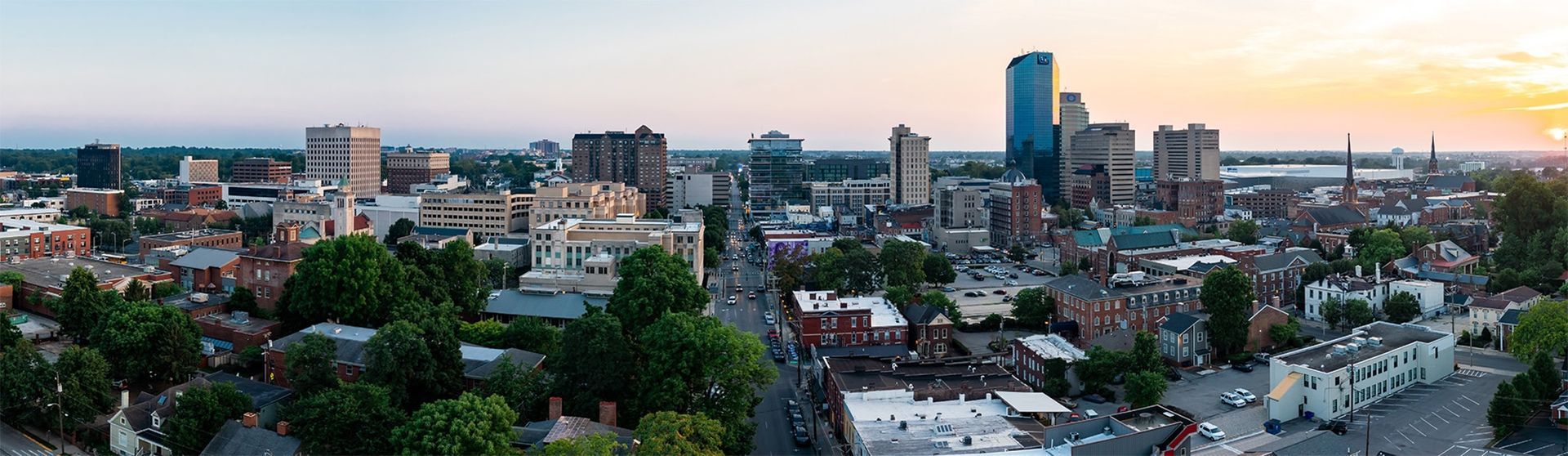 Panoramic aerial view of a city skyline at dusk with tall buildings and residential neighborhoods.