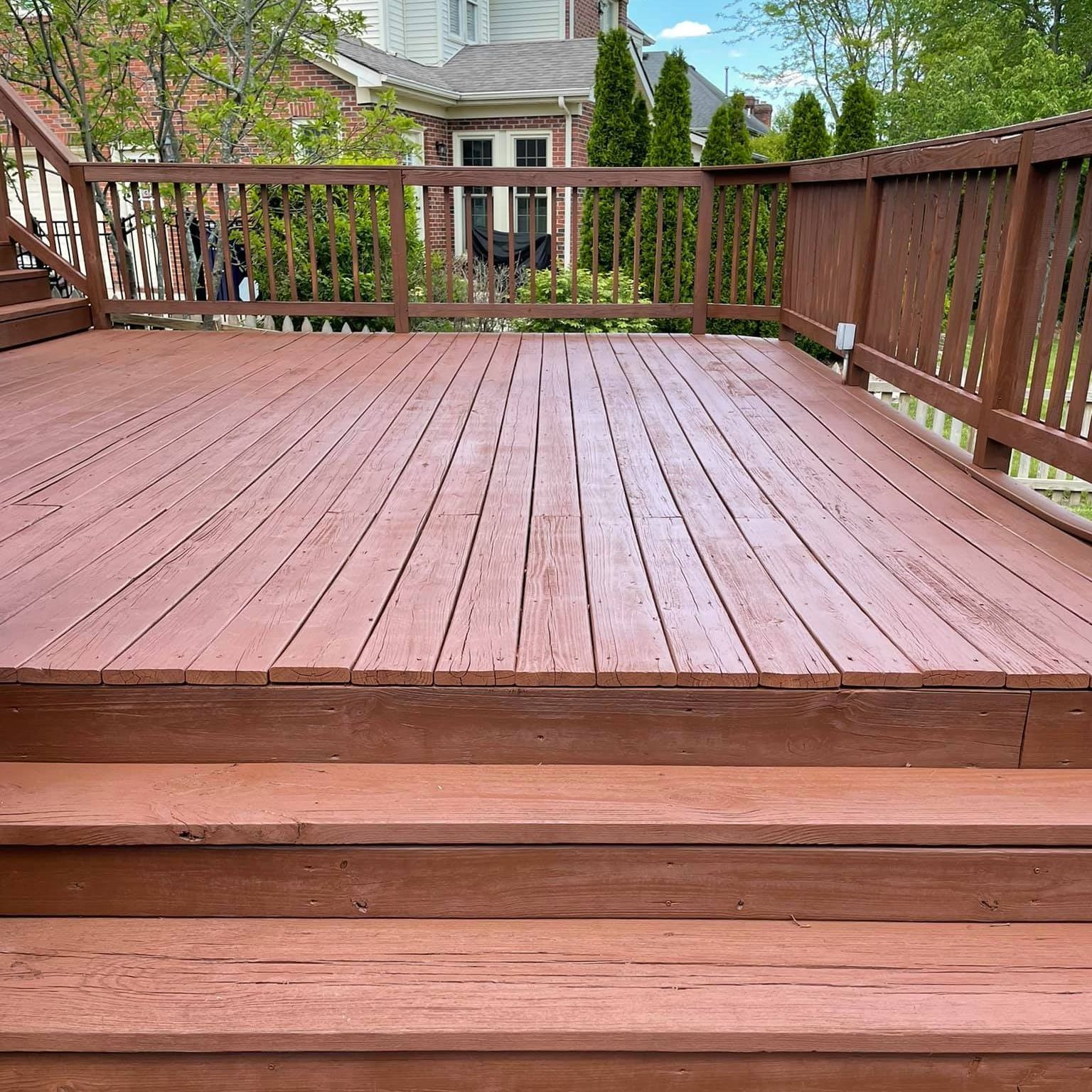Person power washing a brown garage door. House exterior with light siding, flowers, and a porch.