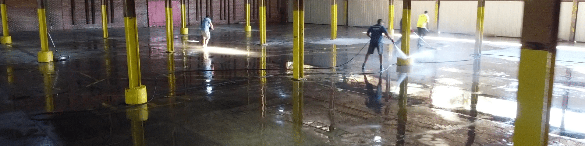 People washing a flooded interior; yellow supports are in the water. One person in dark clothes is holding a hose.