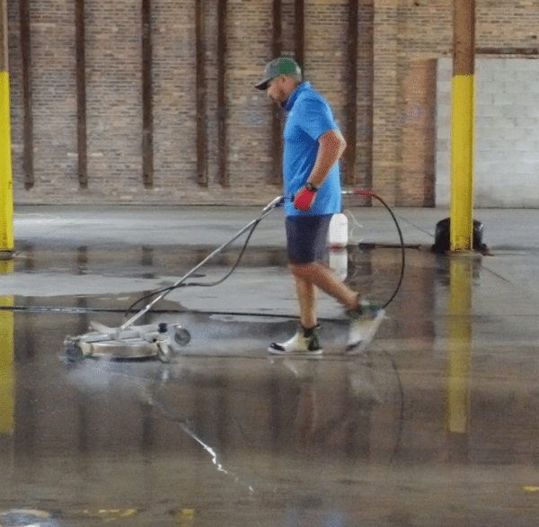 A person using a floor cleaning machine in a large warehouse.