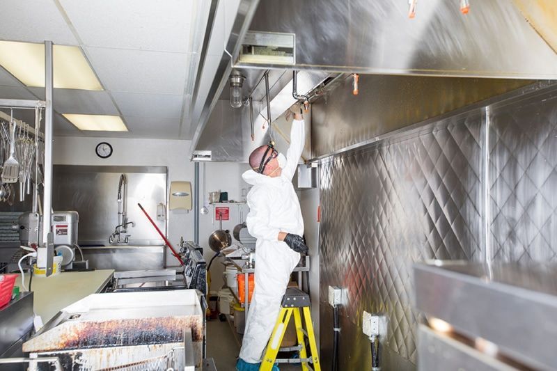 Person in a protective suit cleaning a commercial kitchen vent hood.