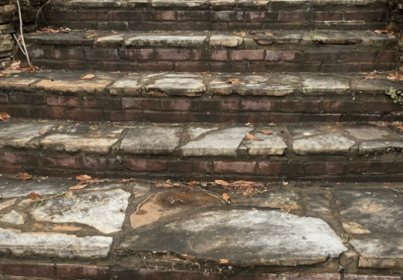 Brick and stone outdoor staircase, weathered and worn, with fallen leaves.