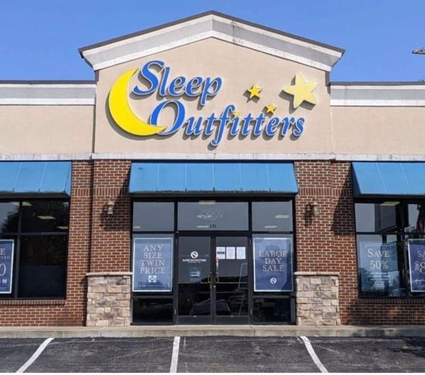 Exterior of a Sleep Outfitters store with sign, blue awnings, and a brick facade.