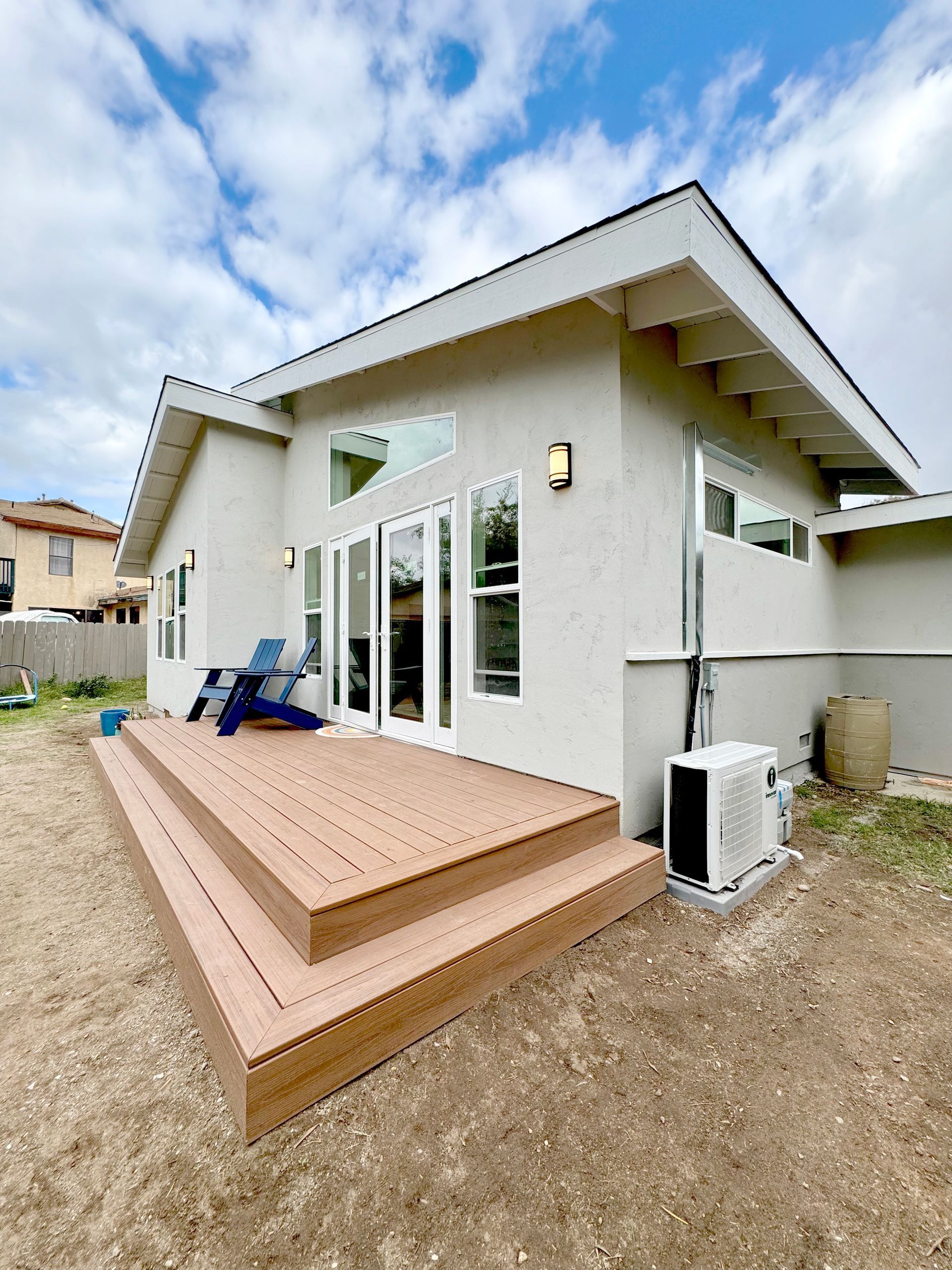 Backyard deck with three steps, leading to a house with large windows and a white exterior under a cloudy sky.
