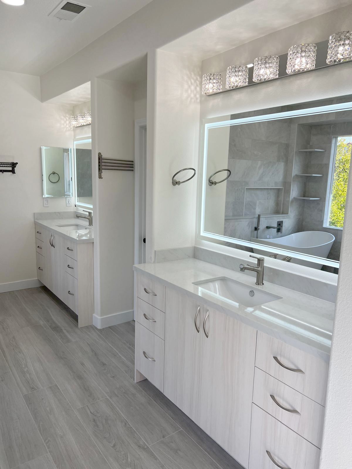 Modern white bathroom with two vanities, sinks, mirrors, and light fixtures.