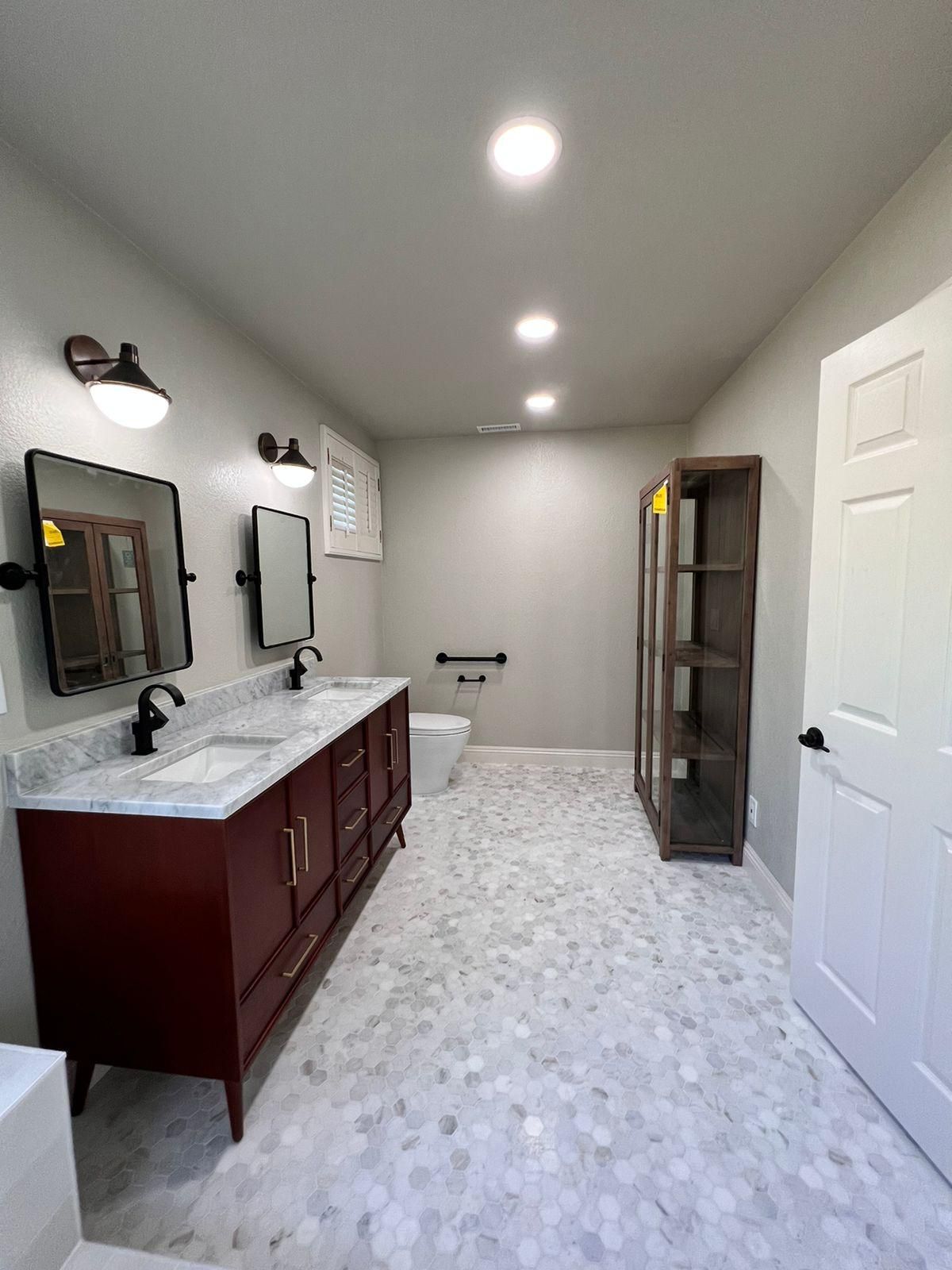A bathroom featuring a burgundy double vanity, two black-framed mirrors, white tile floor, and a tall wooden cabinet.