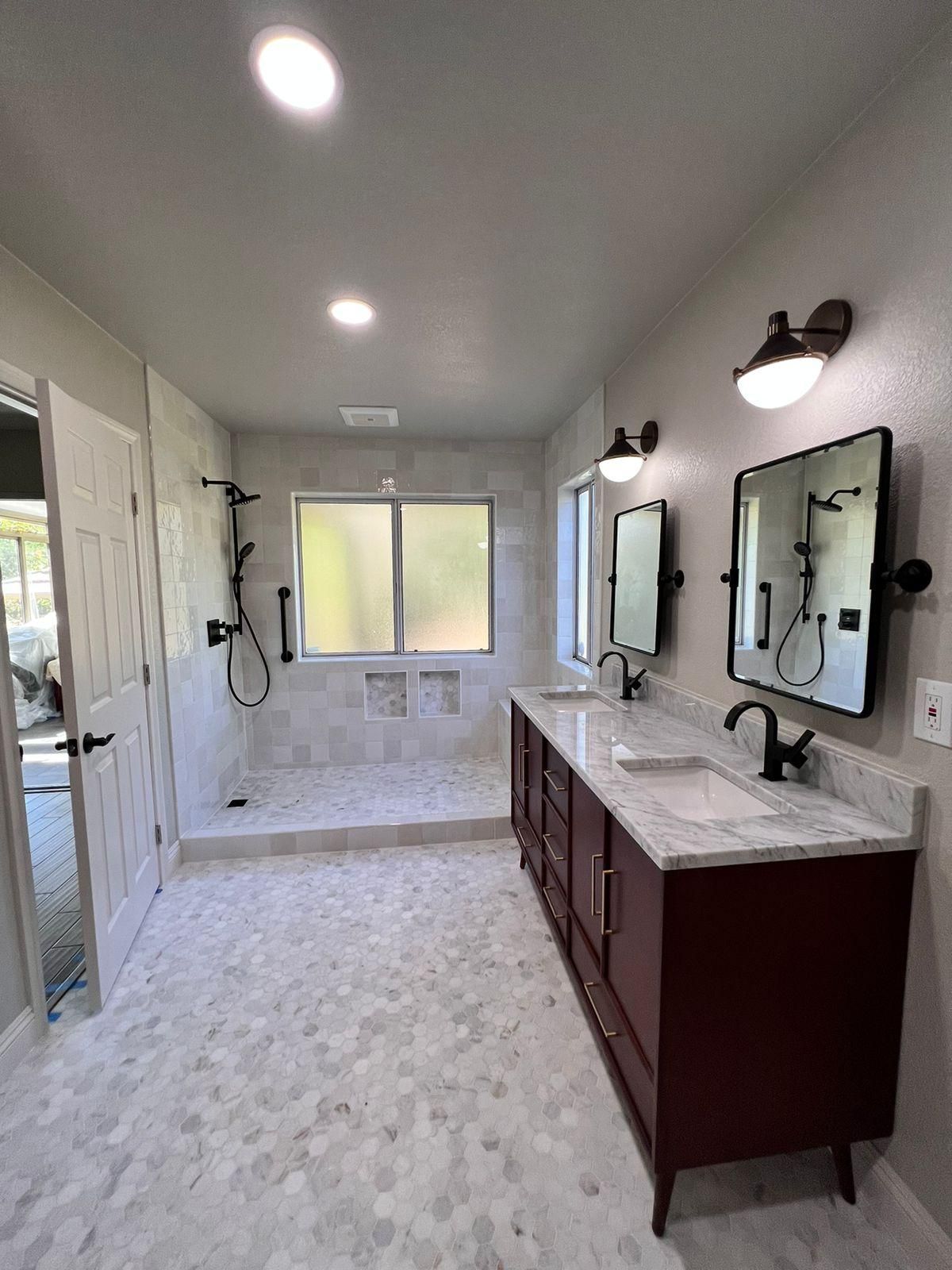 Modern bathroom with dark red vanity, marble countertops, walk-in shower, and black fixtures.