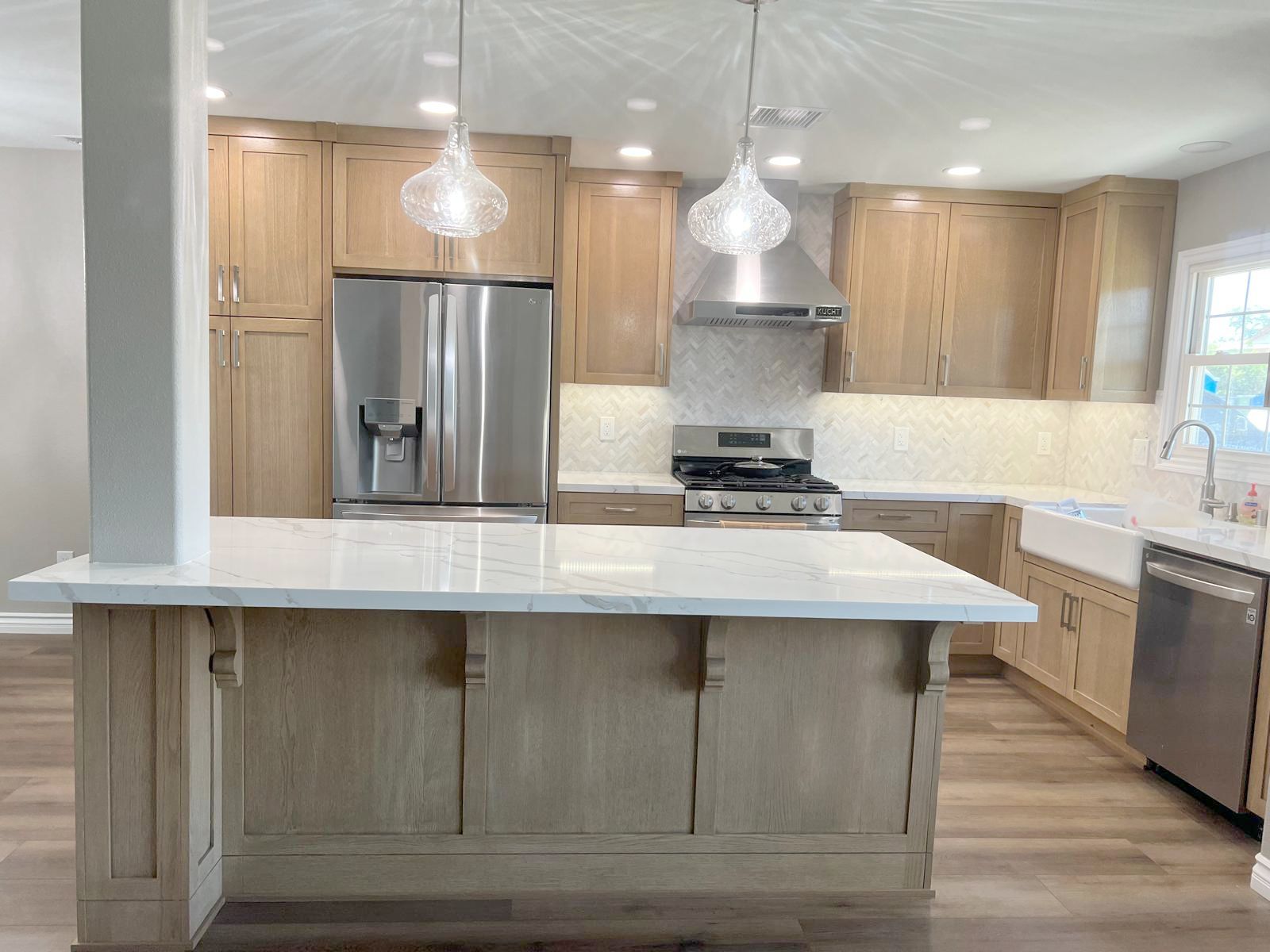 Light oak kitchen with island, stainless steel appliances, and white countertops.