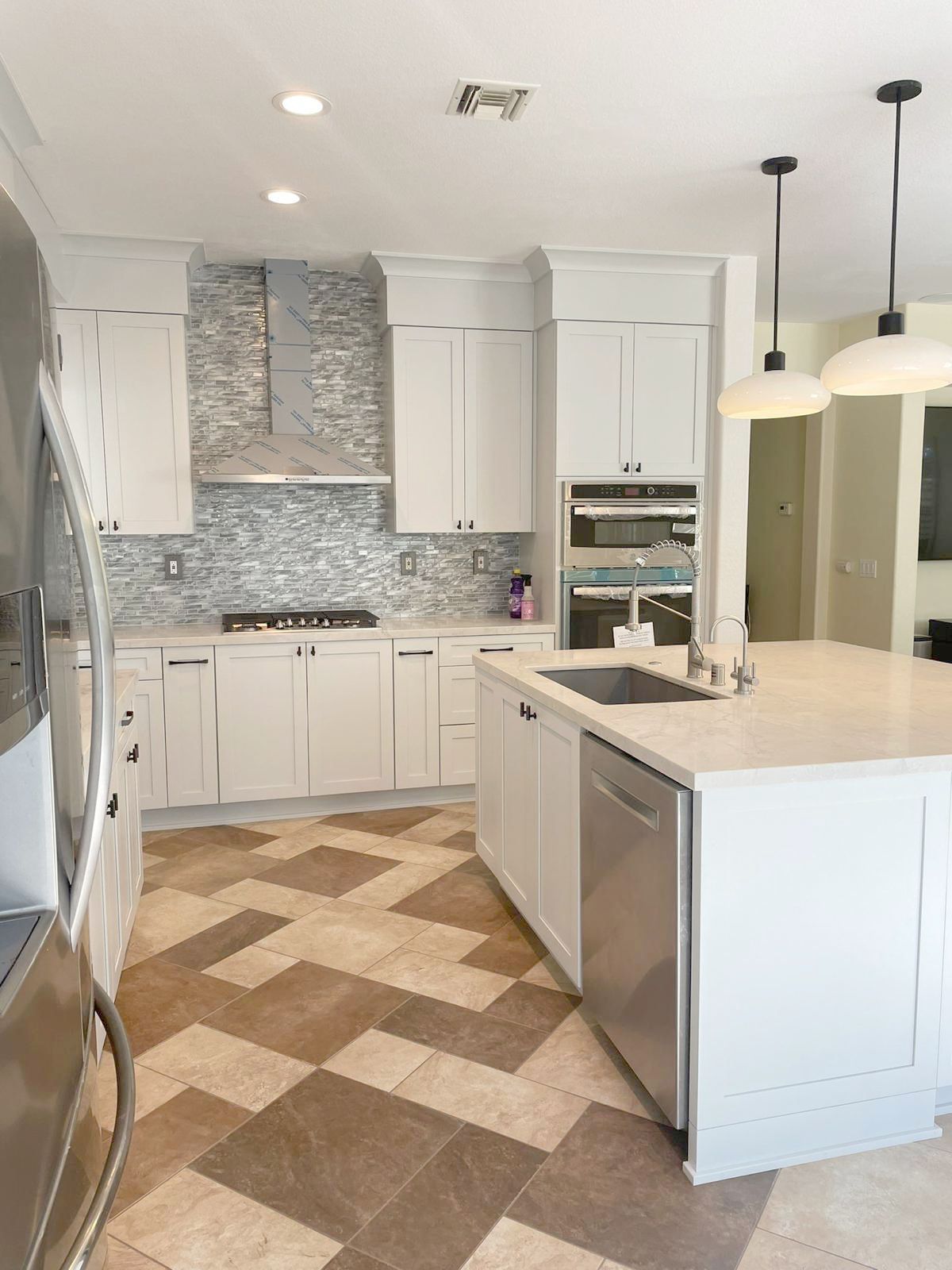 White kitchen with herringbone tile floor, white cabinets, stainless steel appliances, and island.