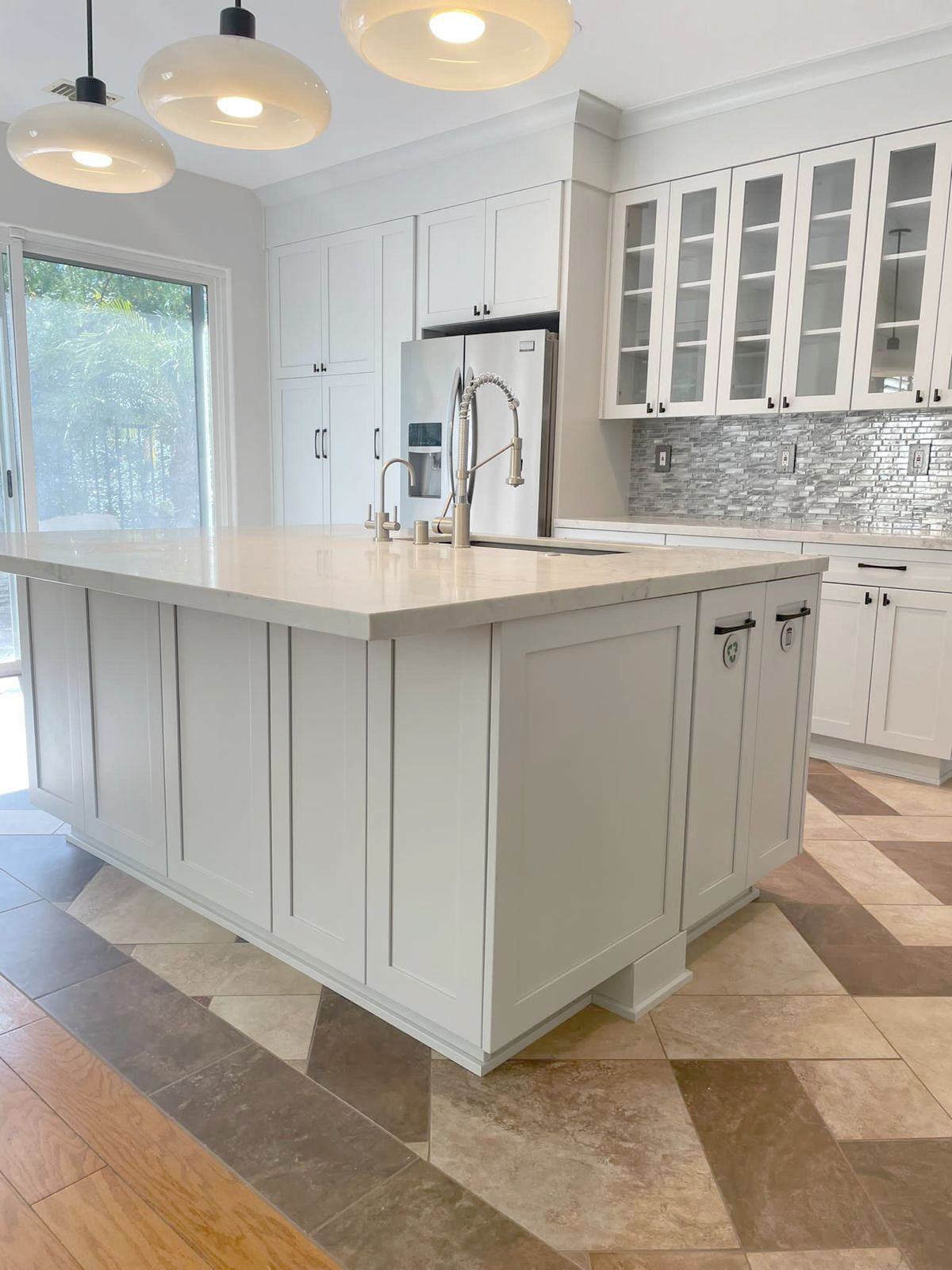 White kitchen with a large island, stainless steel appliances, and patterned floor.