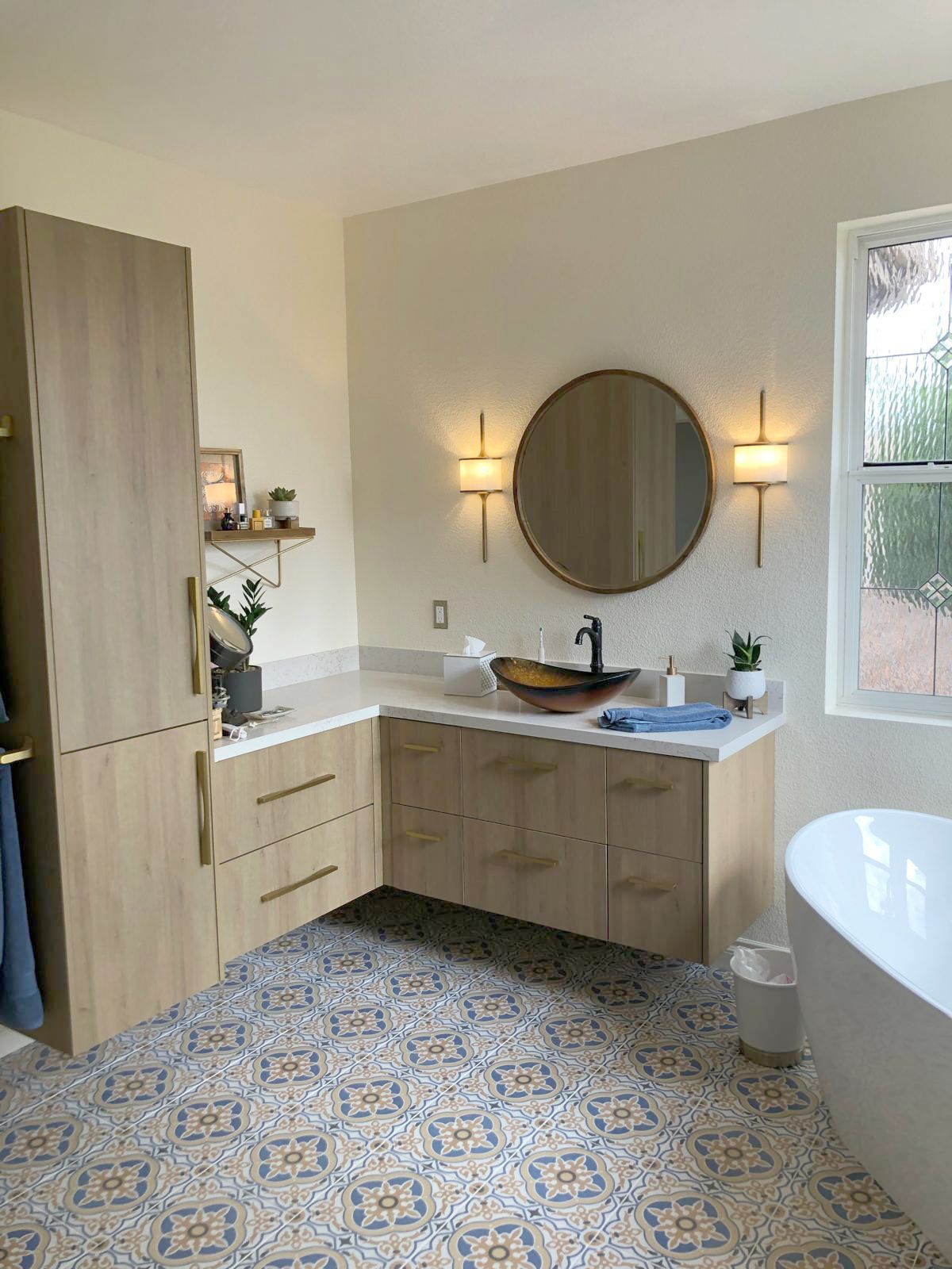 Bathroom with wood cabinets, patterned floor, round mirror, and a bathtub.
