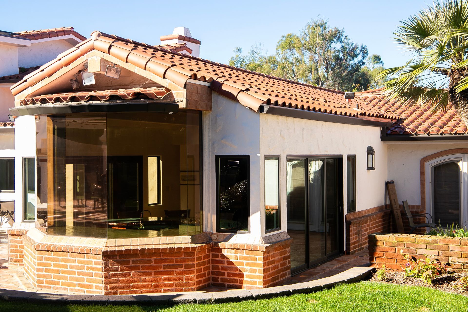 Tan stucco home exterior with red tile roof, brickwork, and large windows.