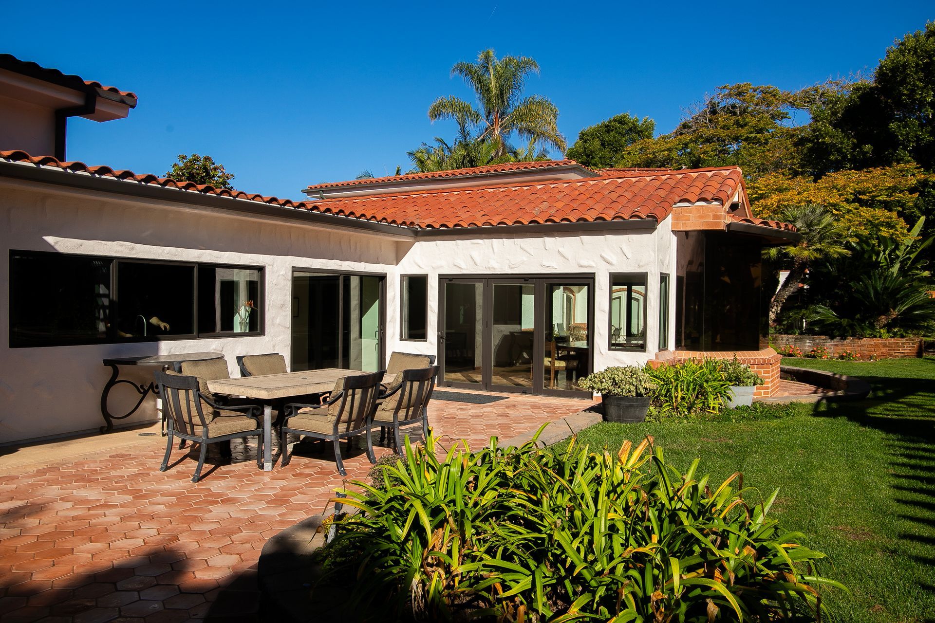 Exterior patio of a house with dining table and chairs, red tile roof, and green lawn.