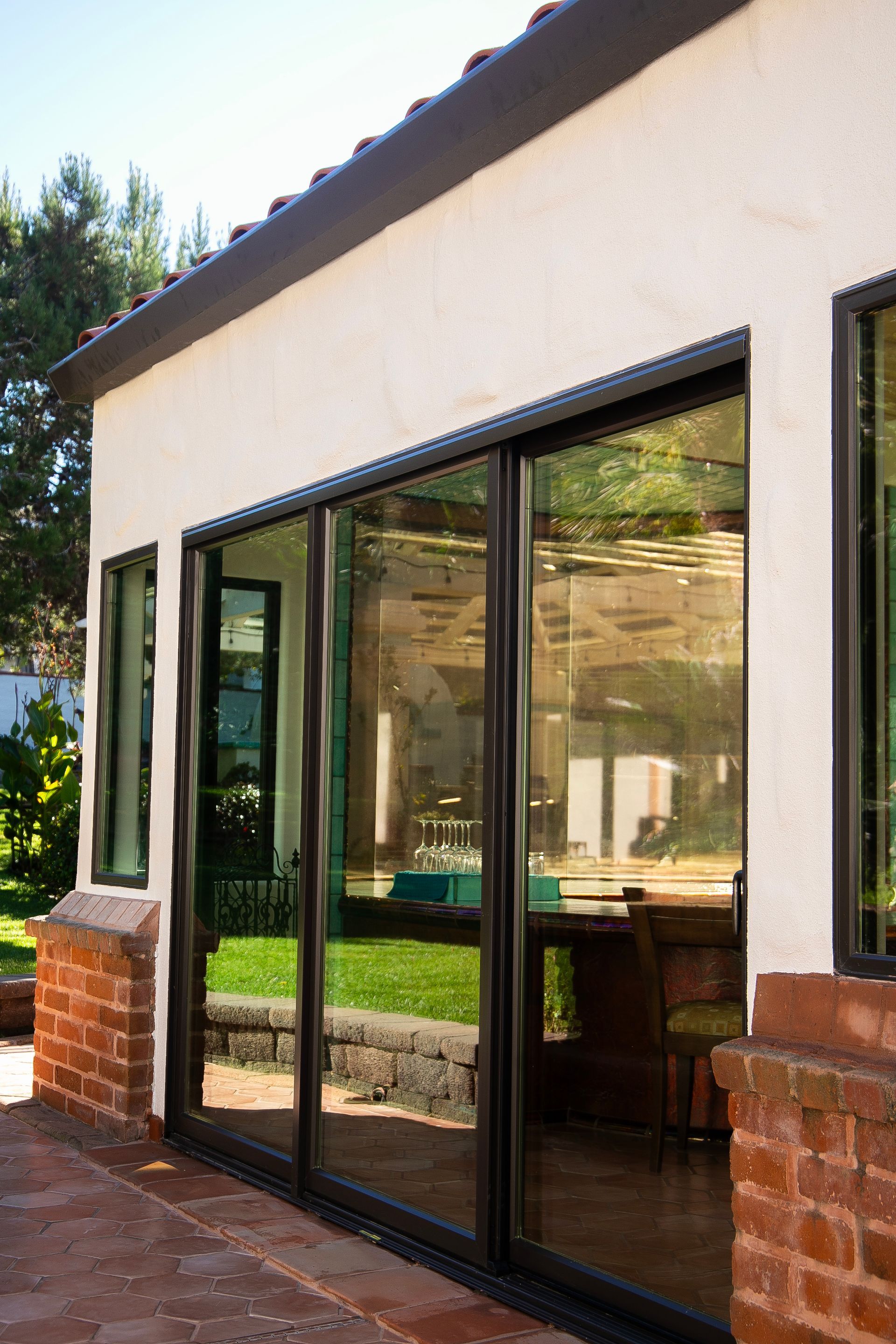 Glass sliding doors on white building with brick accents, reflecting outdoor patio and yard.
