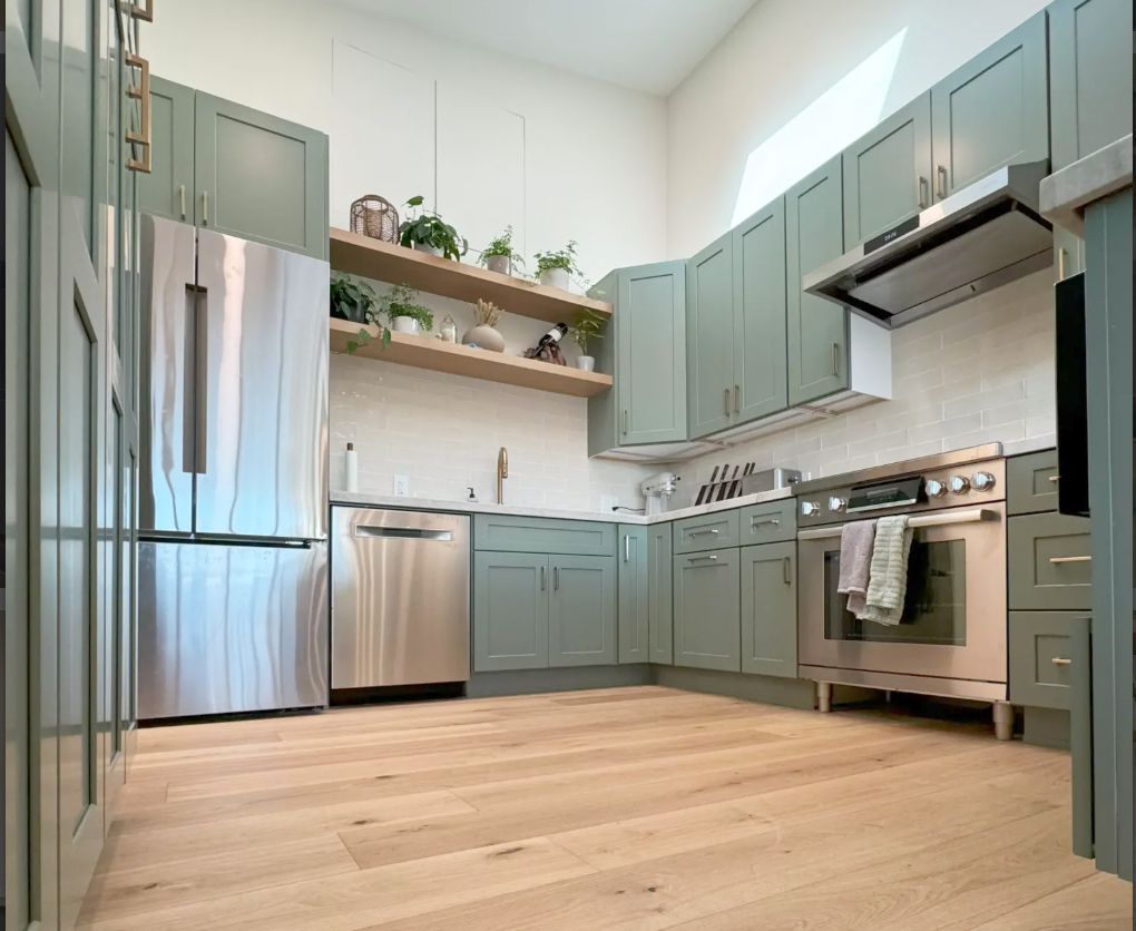 Modern kitchen with sage green cabinets, stainless steel appliances, and wood flooring.