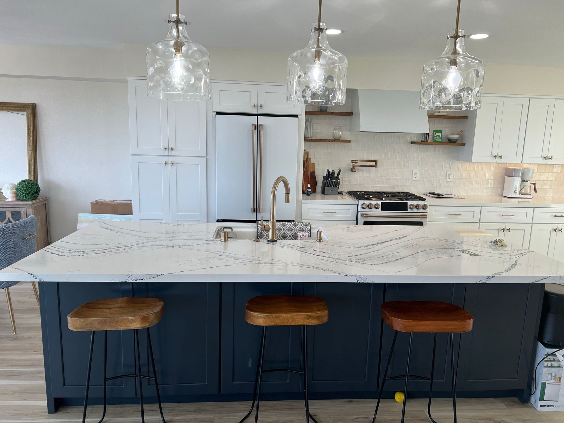 Kitchen with navy island, white countertops, and three pendant lights. Three wooden stools and a stainless steel range.