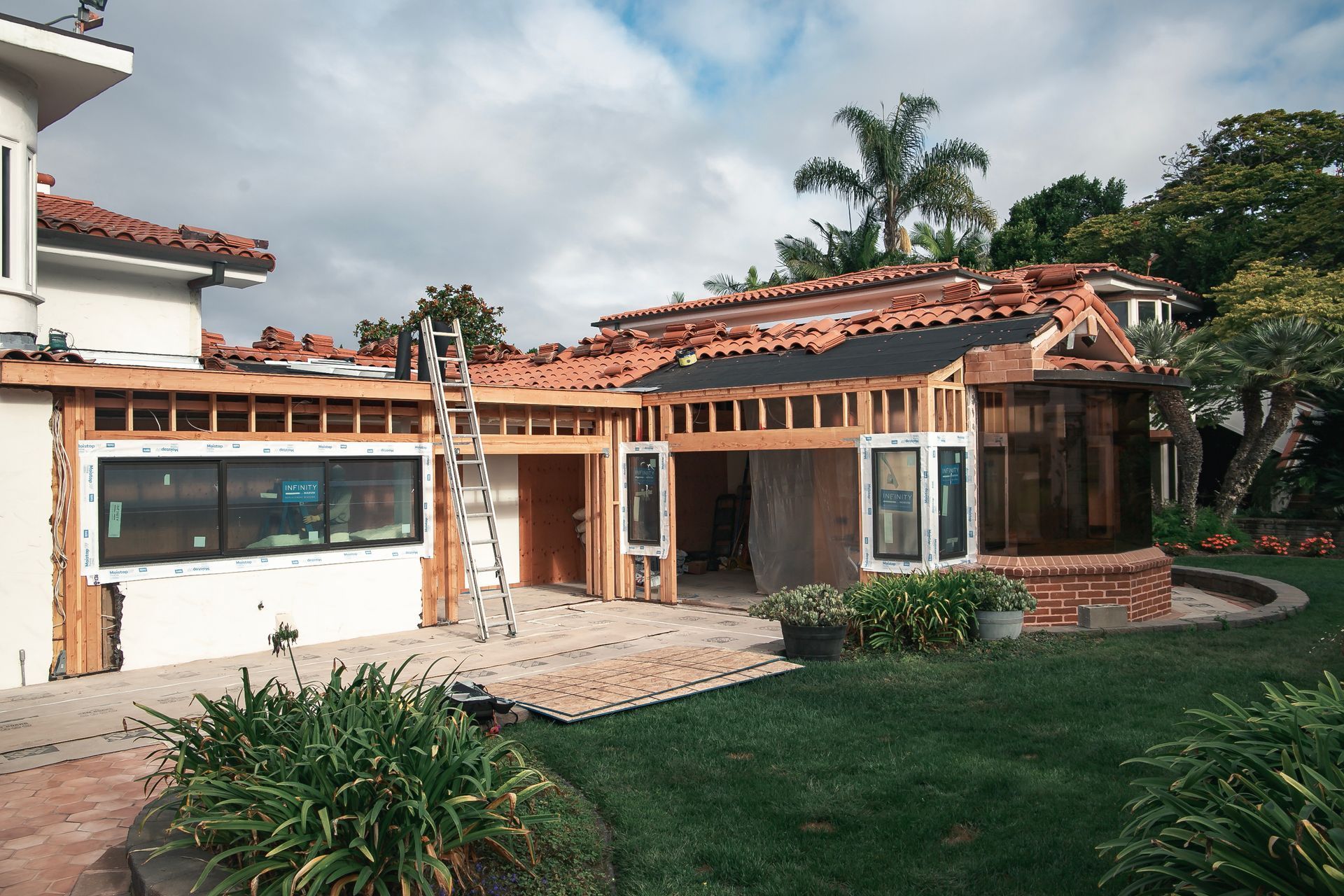 House under construction with exposed framing, red tile roof, and a green lawn.