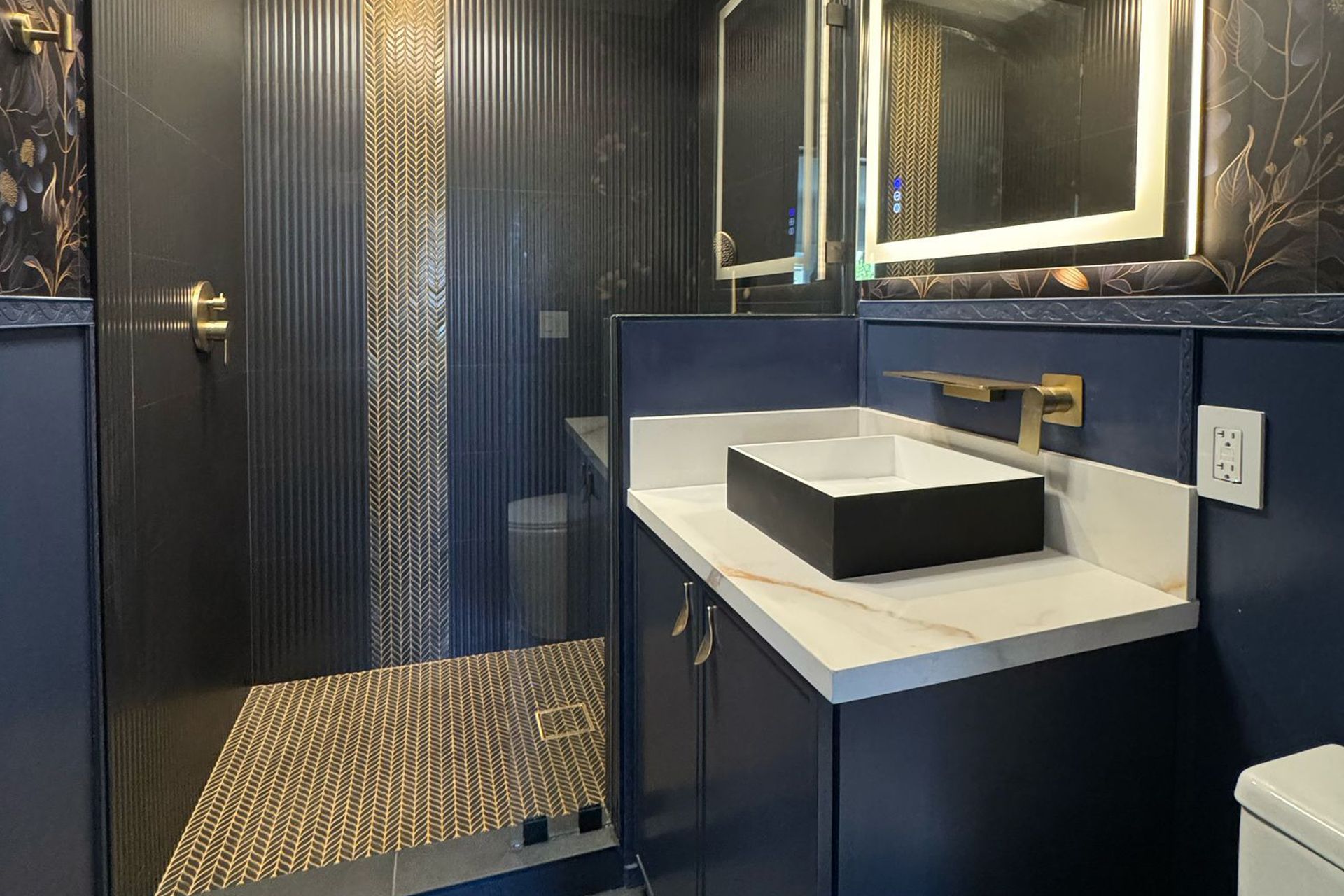 Modern bathroom with navy blue walls, gold accents, marble countertops, black vessel sink.