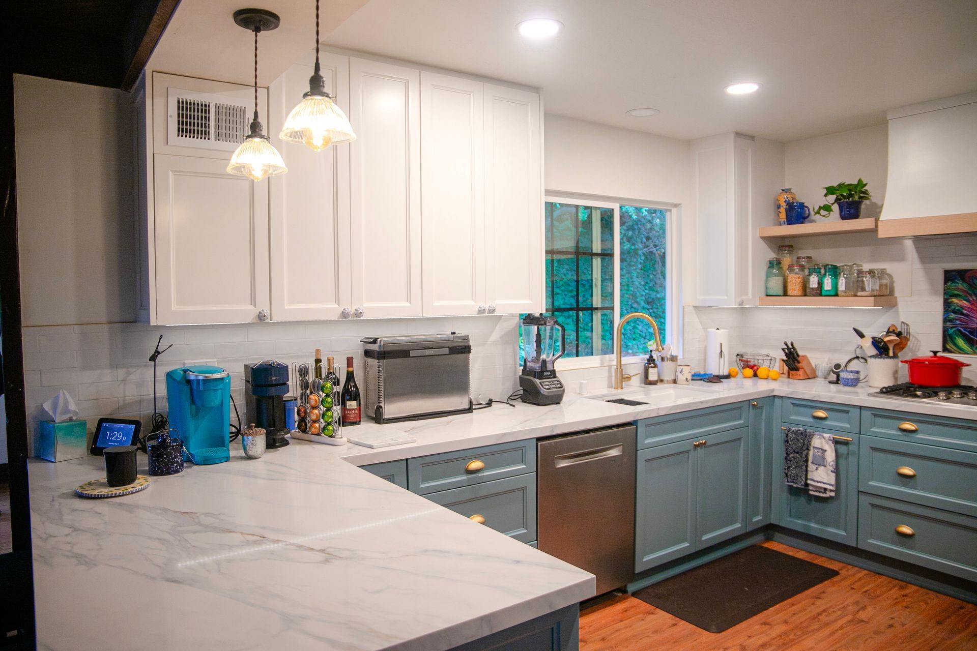 U-shaped kitchen with white and blue cabinets, marble countertops, stainless steel appliances, and wood flooring.