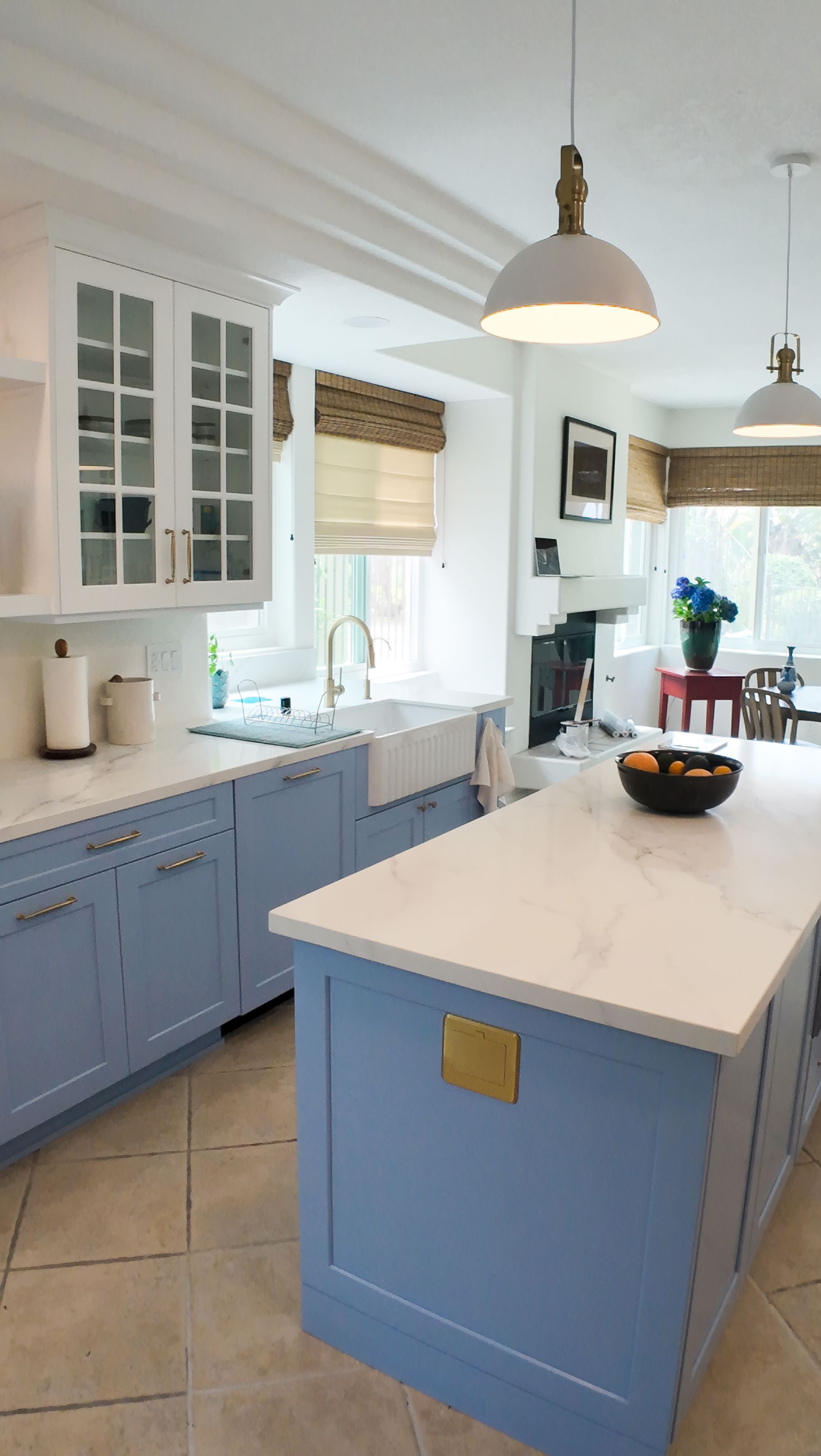 Blue and white kitchen with island, white countertops, farmhouse sink, and cream-colored tile floor.
