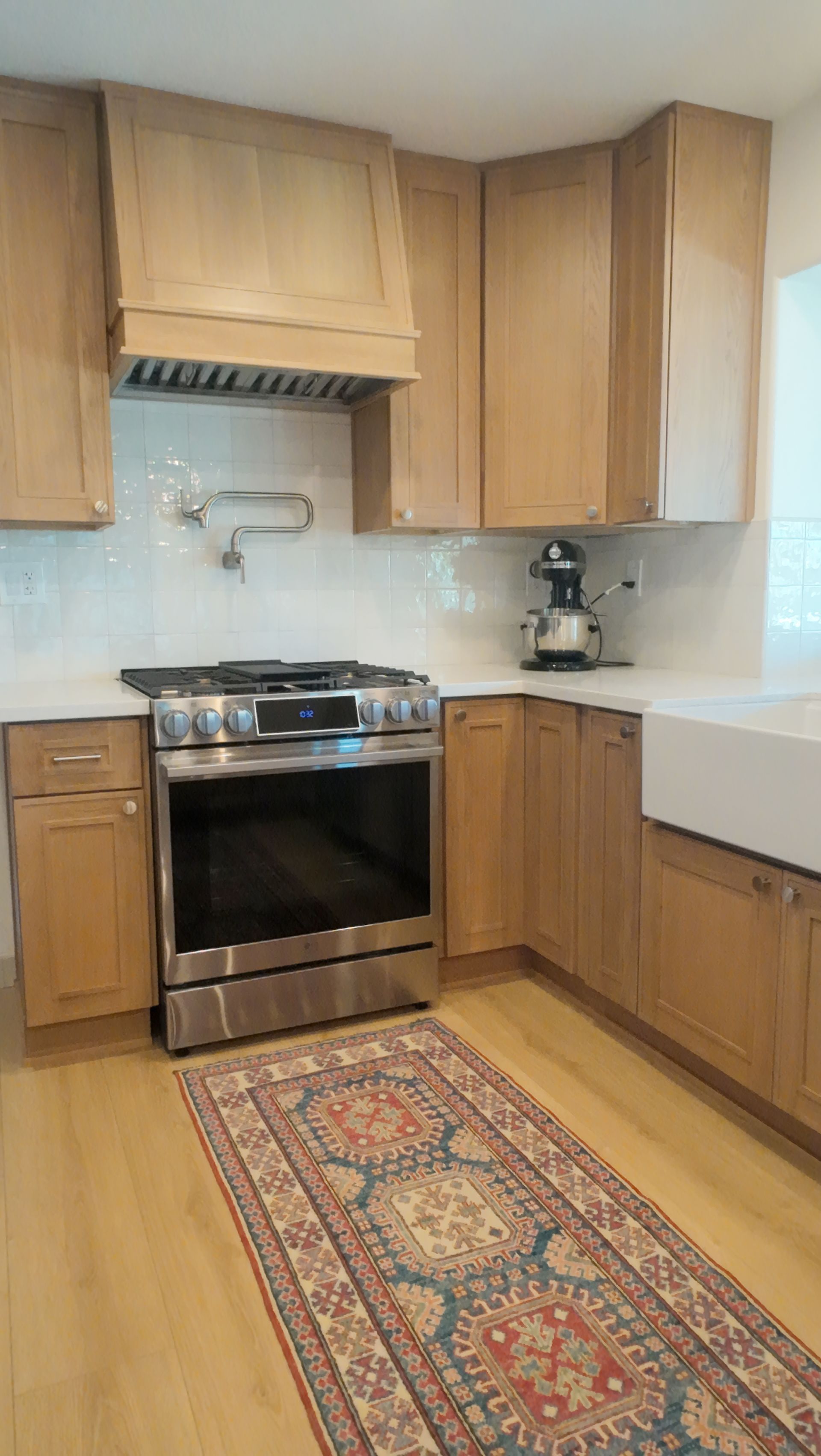 Kitchen with light wood cabinets, stainless steel stove, and colorful rug.