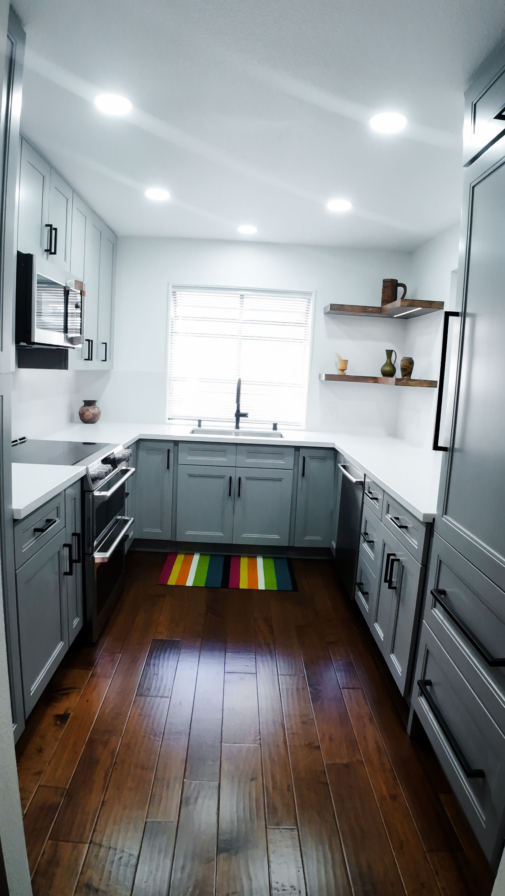 Gray and white modern kitchen with island, wood floors, and rainbow rug.