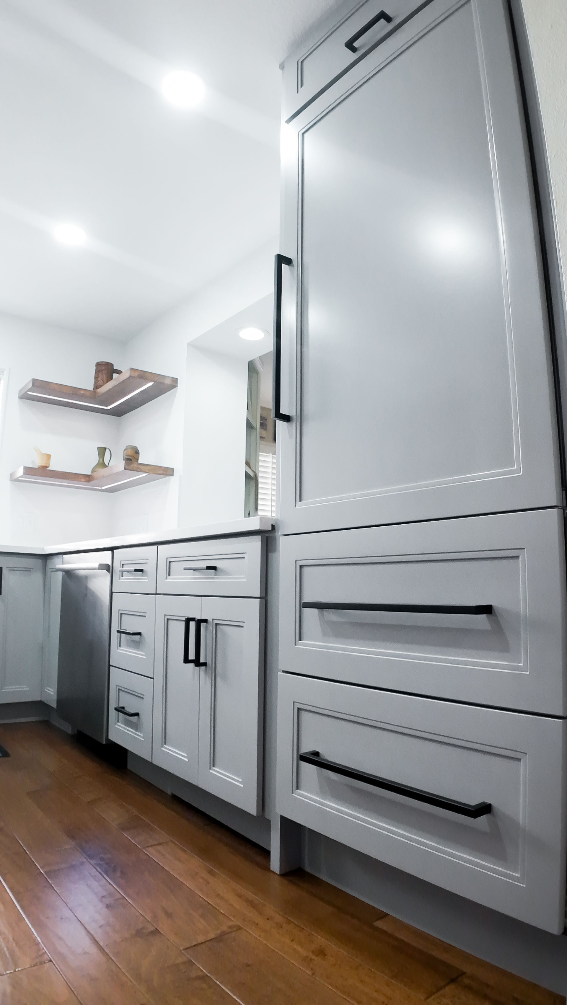 Gray kitchen cabinets with black hardware on hardwood floor.