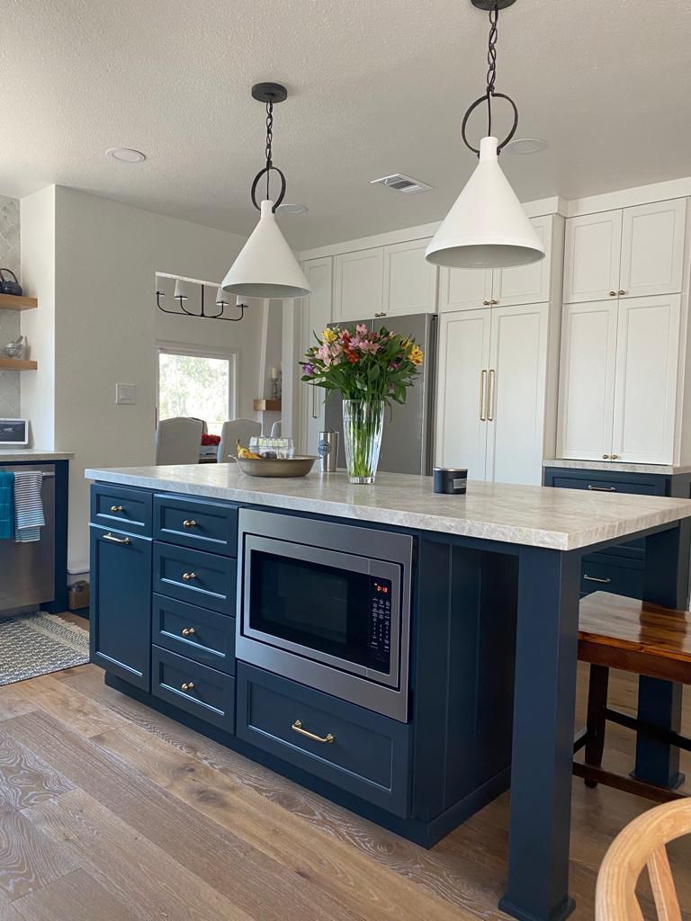 Navy blue kitchen island with a built-in microwave, white countertops, and two pendant lights.