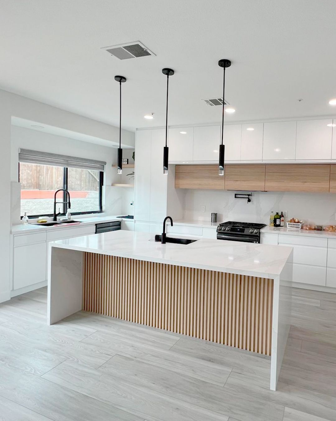 Modern white kitchen with a light wood island, black faucet, and pendant lights.