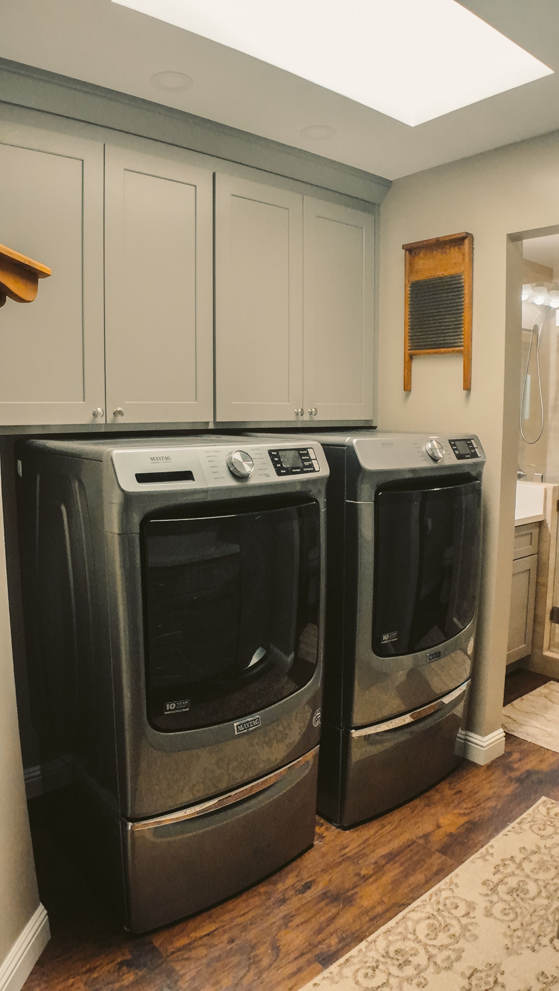 Laundry room with grey cabinets, washer, dryer, and wooden floor.