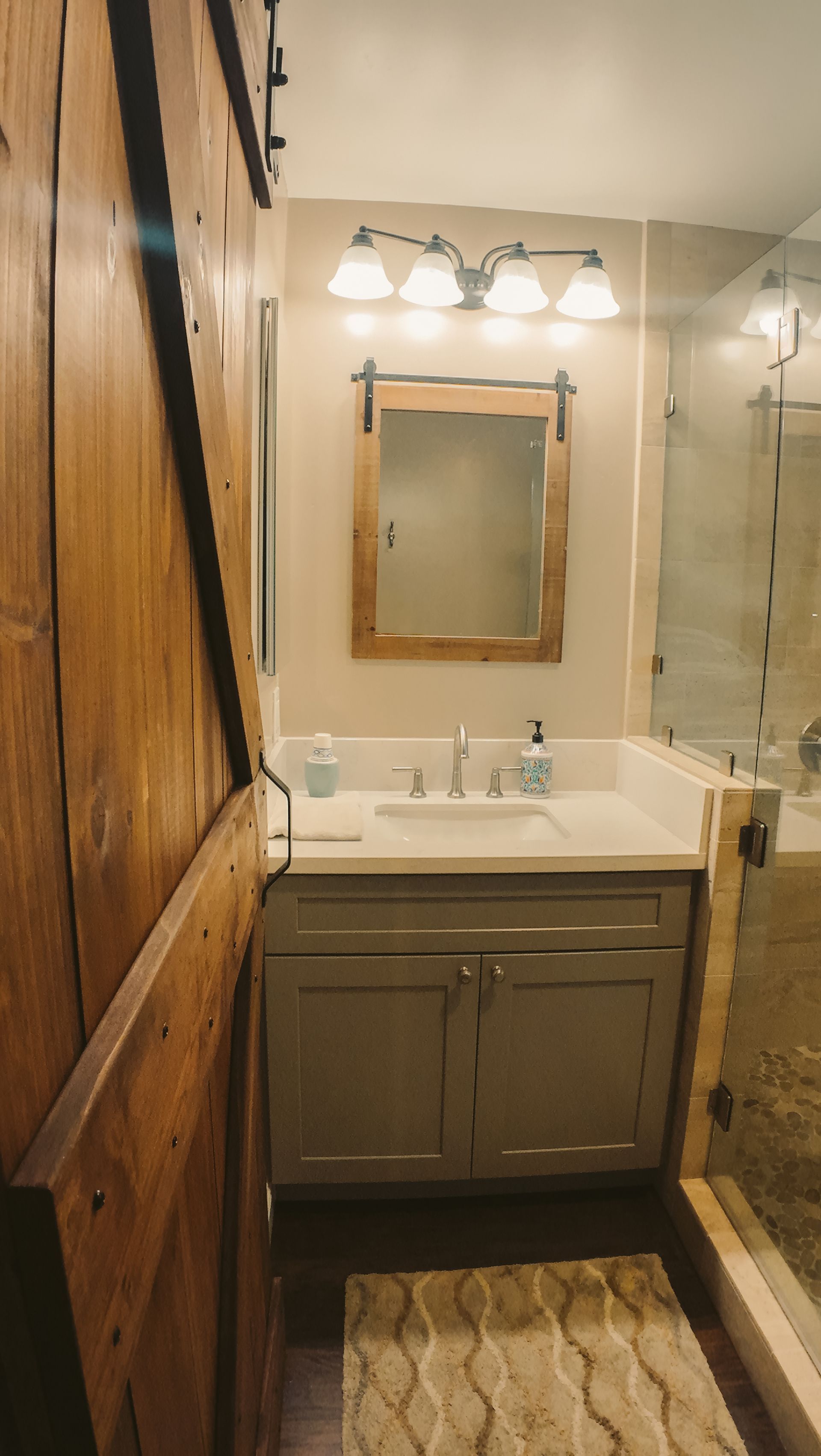 Bathroom with gray vanity, wooden mirror, glass shower, and barn door.