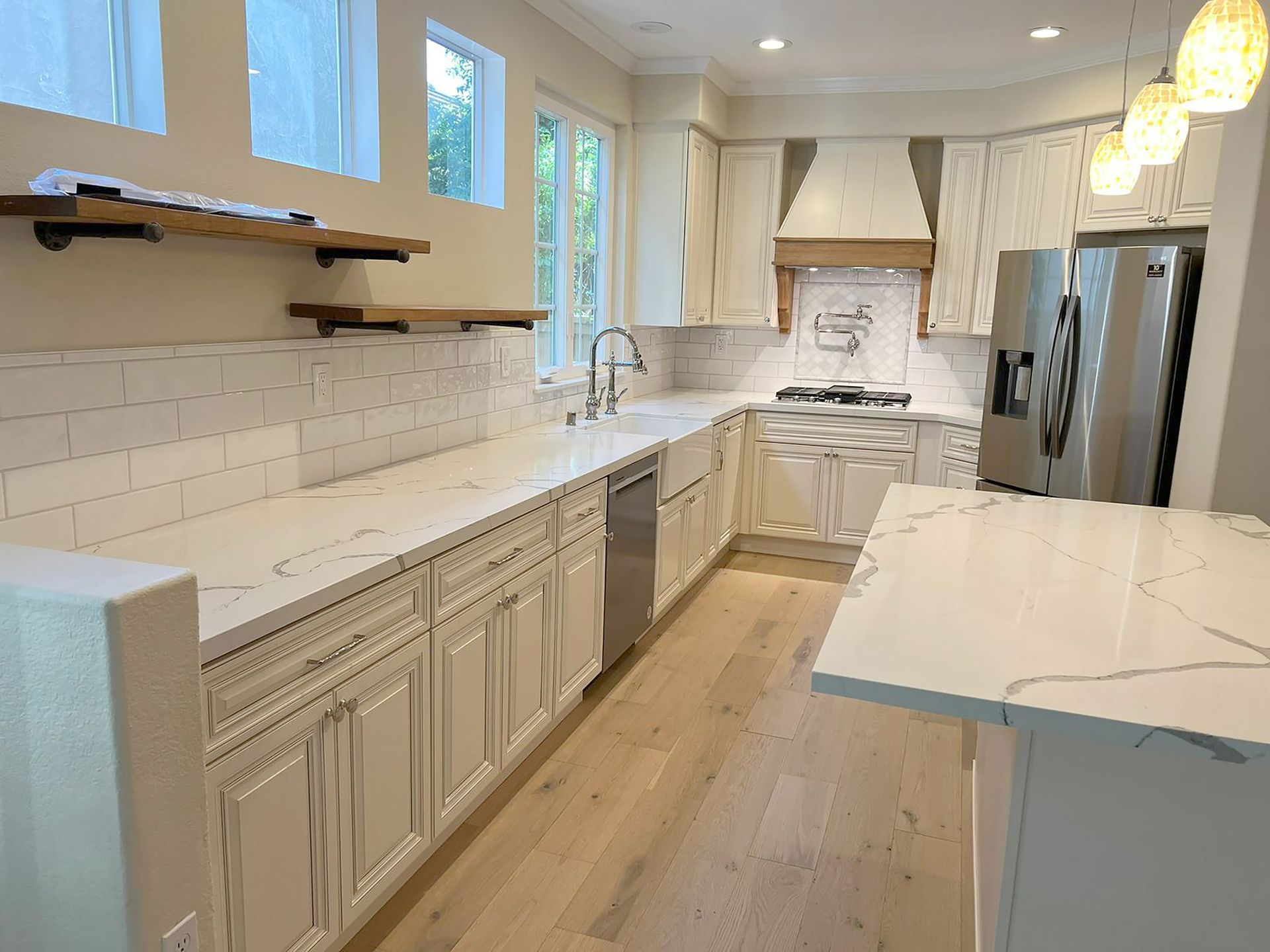 Modern kitchen with white cabinets, countertops, and stainless steel appliances; light wood flooring.