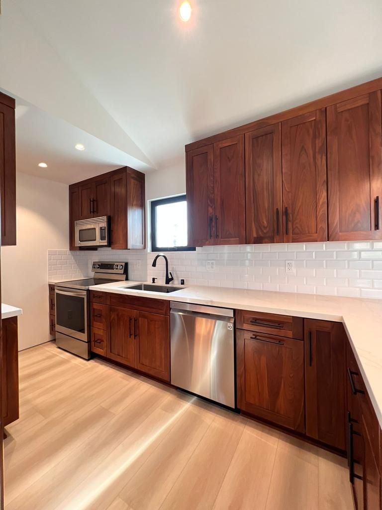 Modern kitchen with wood cabinets, stainless steel appliances, and white countertops.