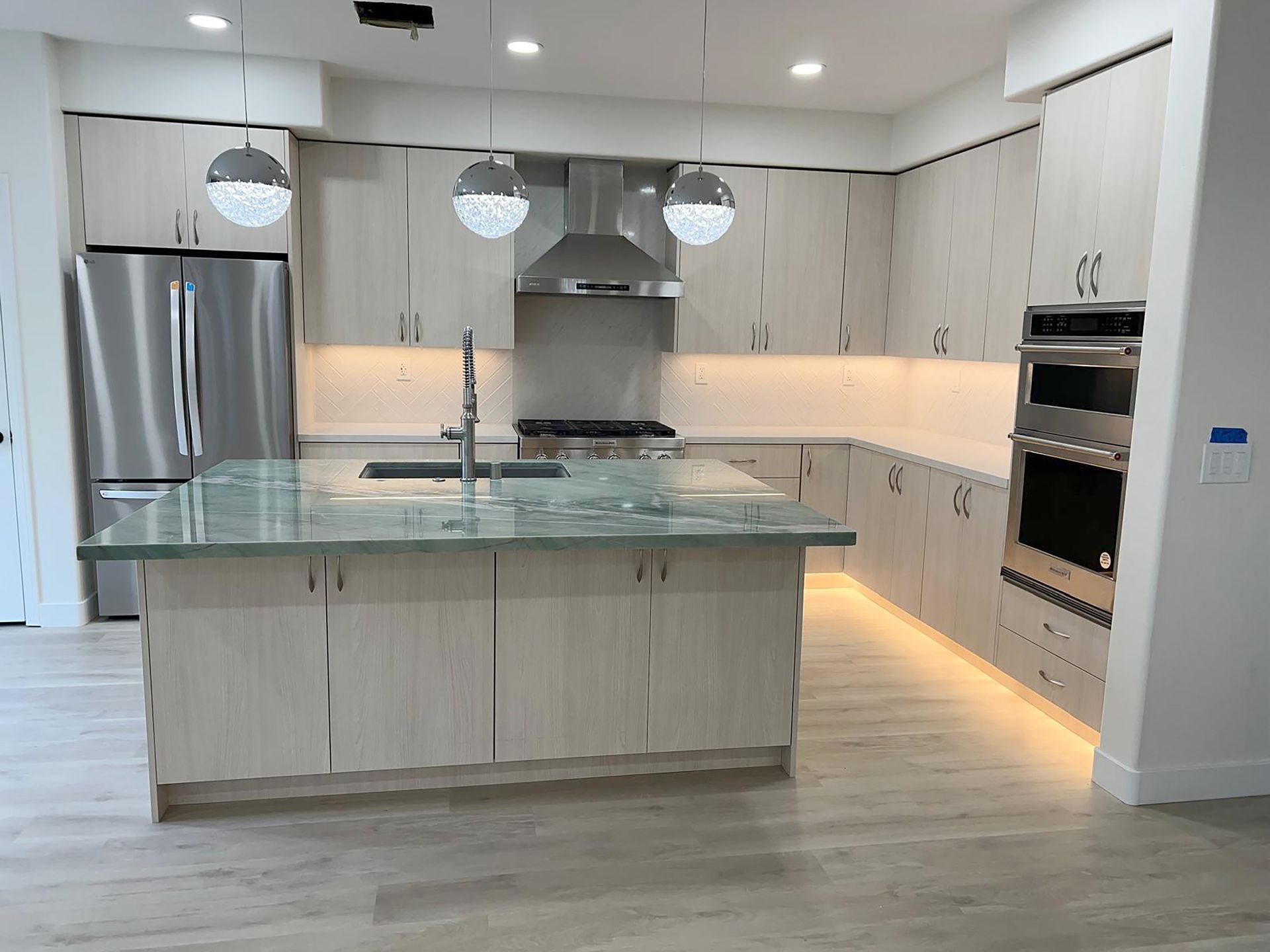 Modern kitchen with light wood cabinets, green island countertop, and stainless steel appliances.