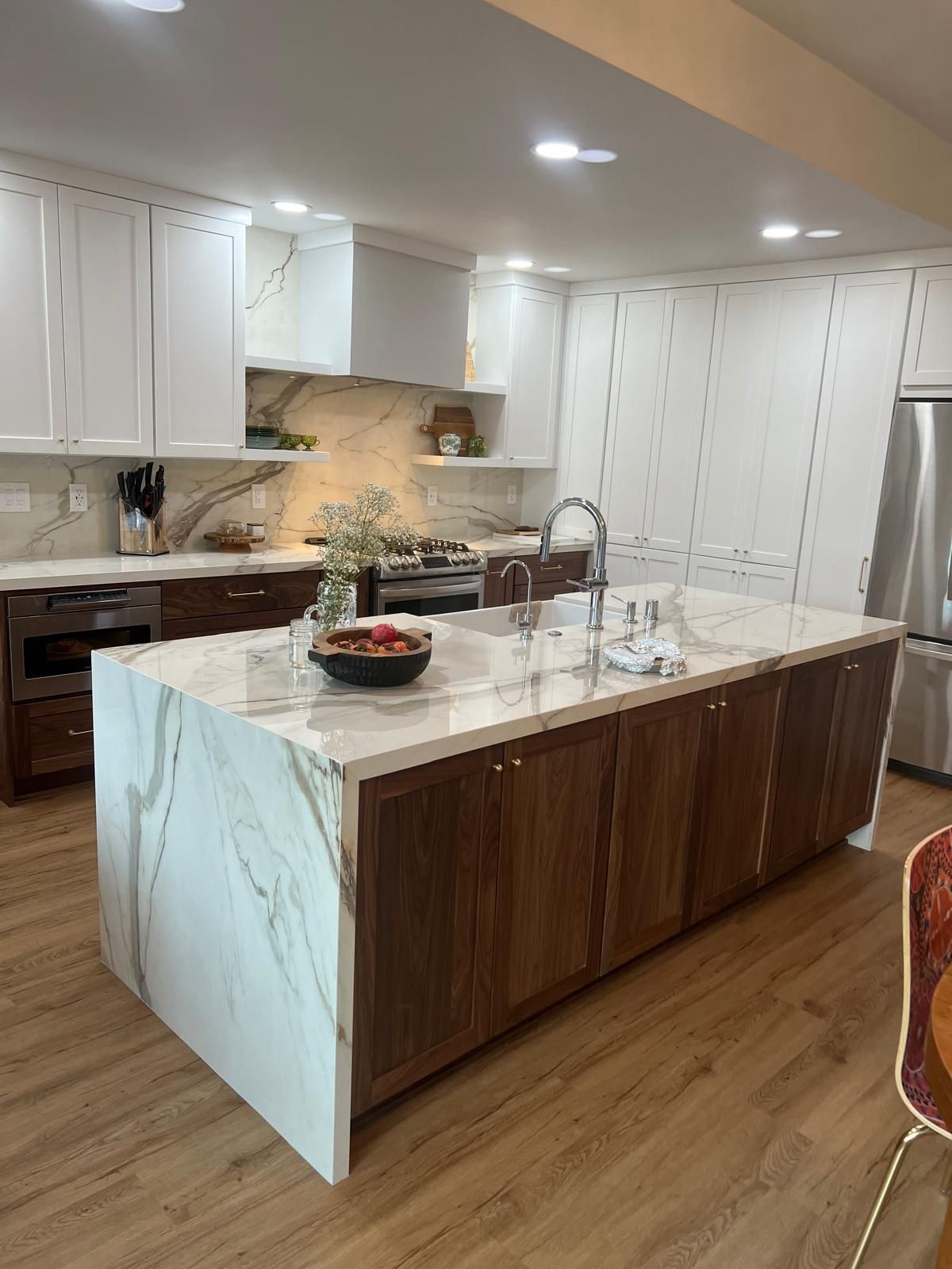 Modern kitchen with white and dark wood cabinets, marble countertops, island with sink, and stainless steel appliances.