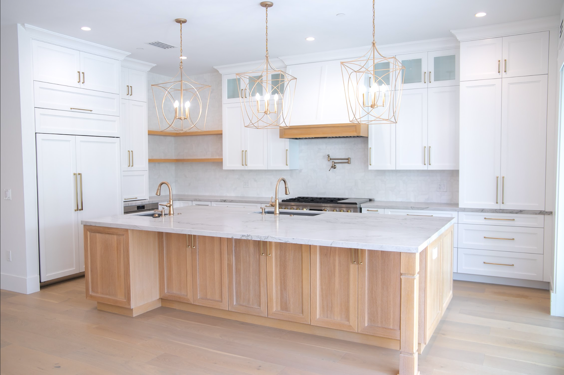 Elegant white kitchen with wooden island, gold hardware, and pendant lights.