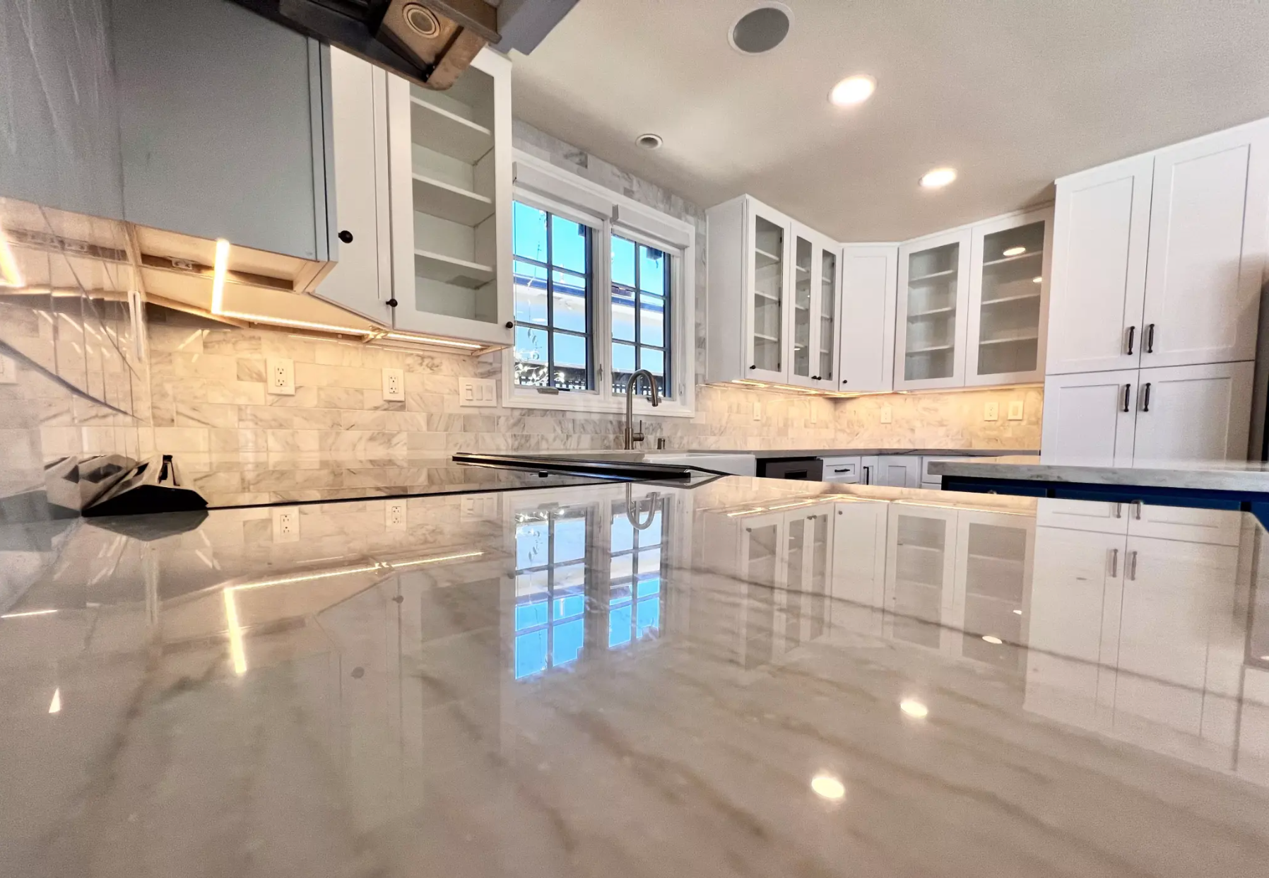 Modern kitchen with island and light wood cabinets, stainless steel appliances, and dark green storage.