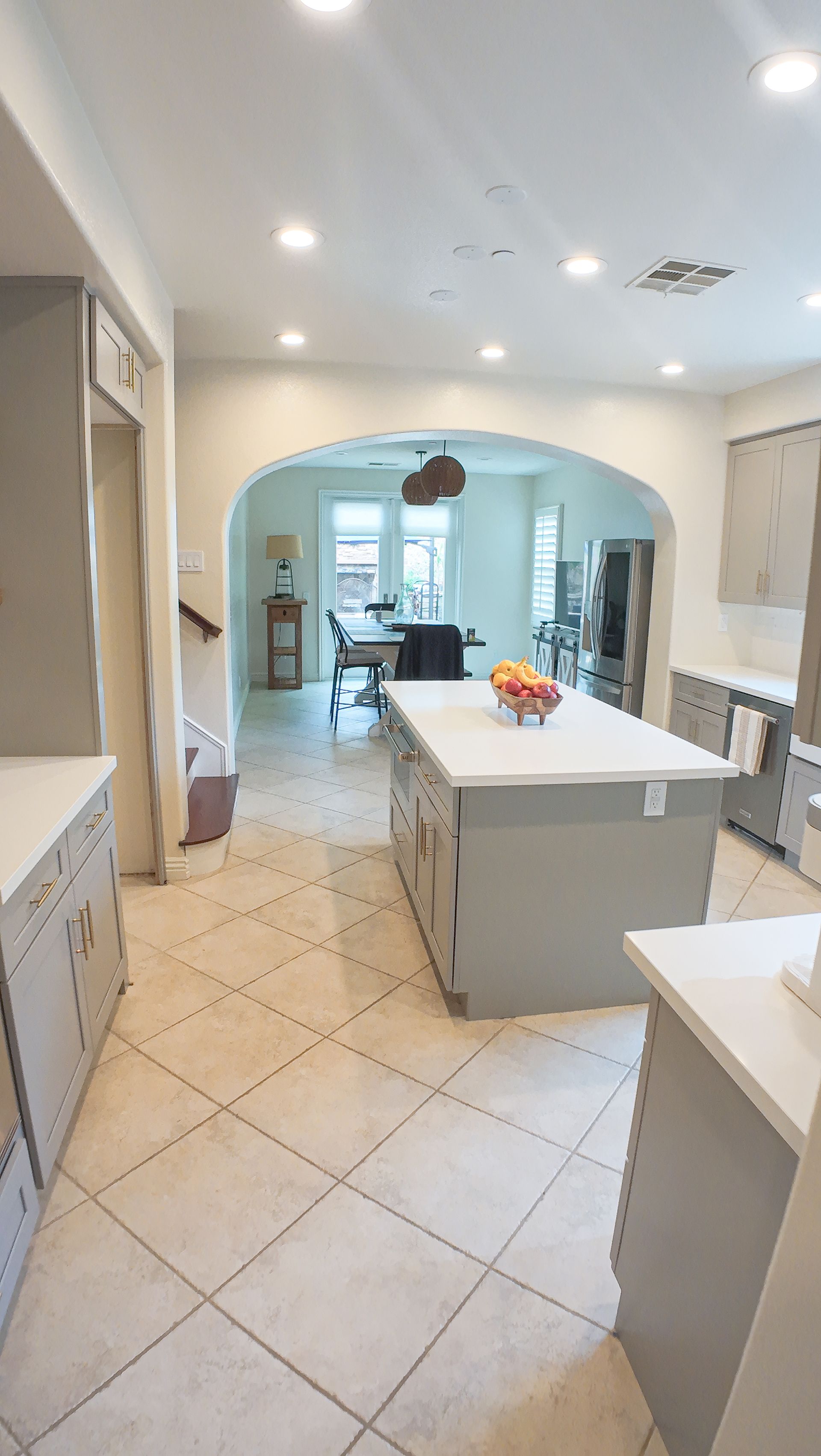 Spacious gray kitchen with a large island, archway to dining room, and tiled floor.