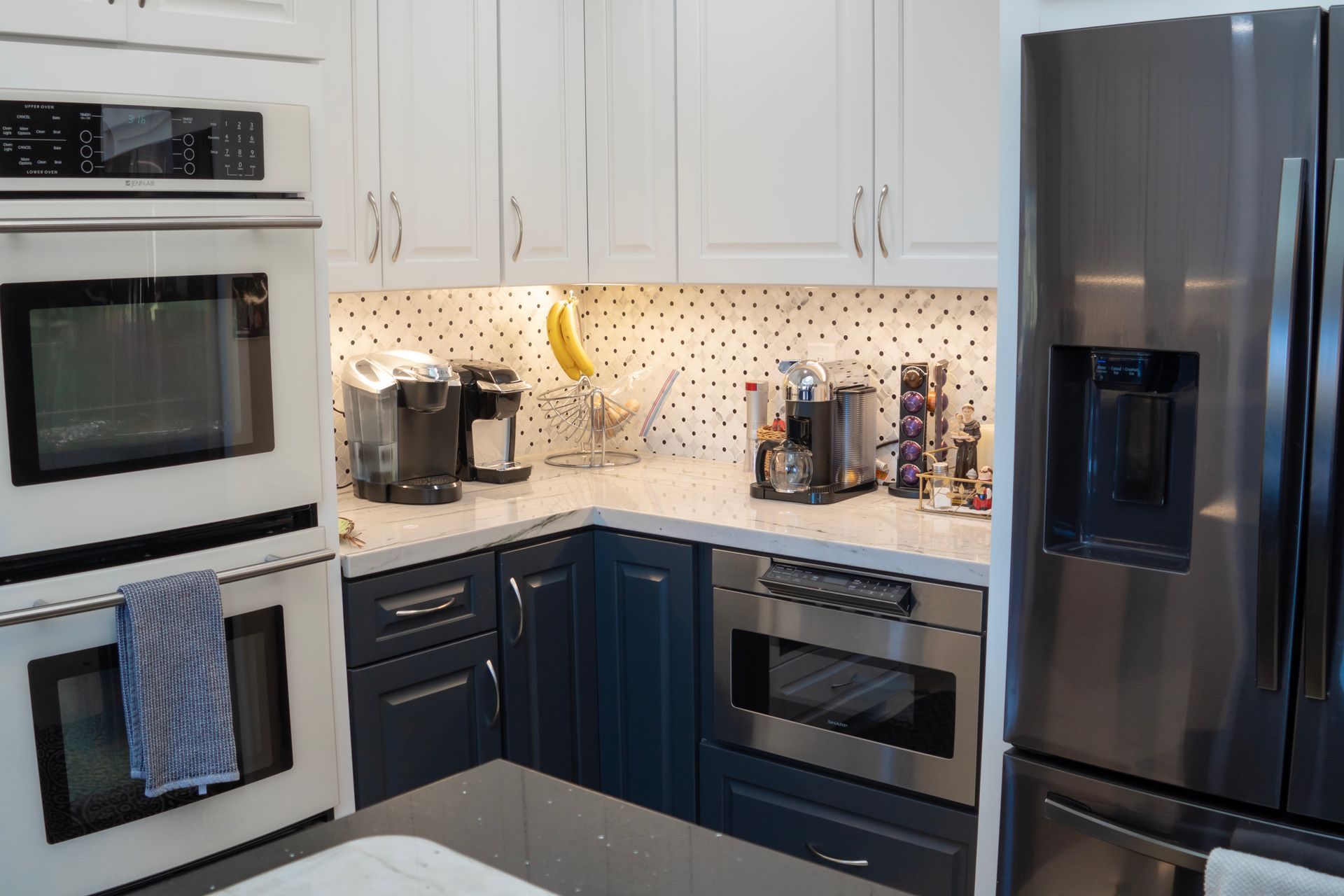Modern kitchen with white and navy cabinets, stainless steel appliances, and black and white backsplash.
