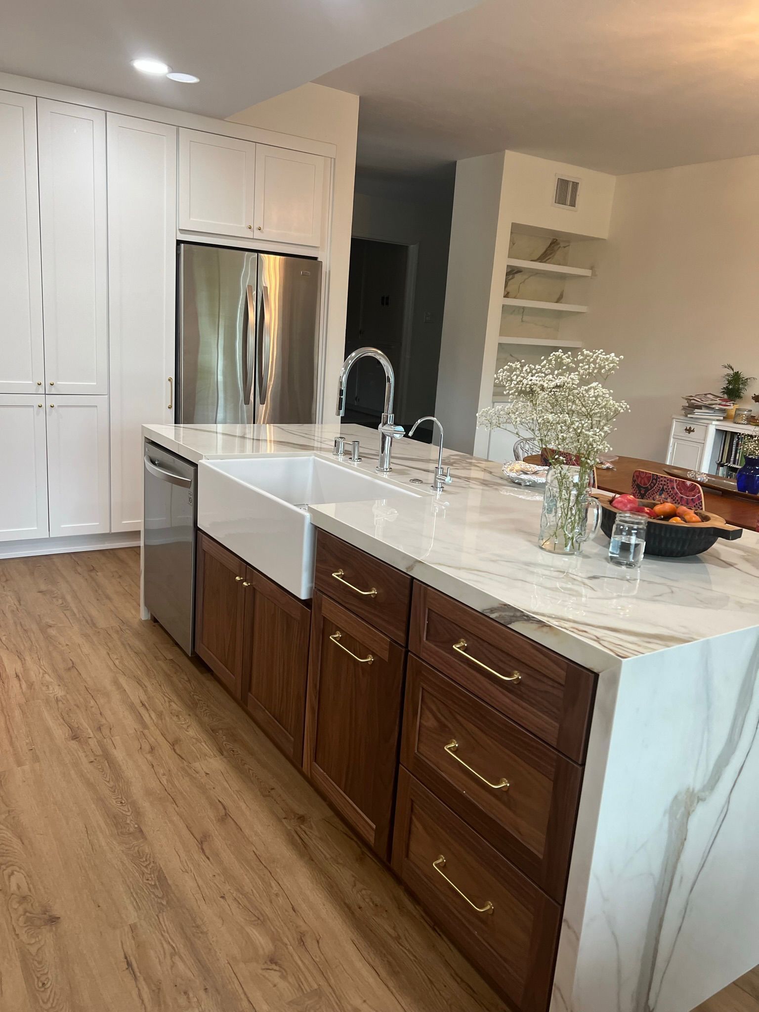Kitchen with a white farmhouse sink on a marble-topped island with dark wood cabinets and stainless steel appliances.