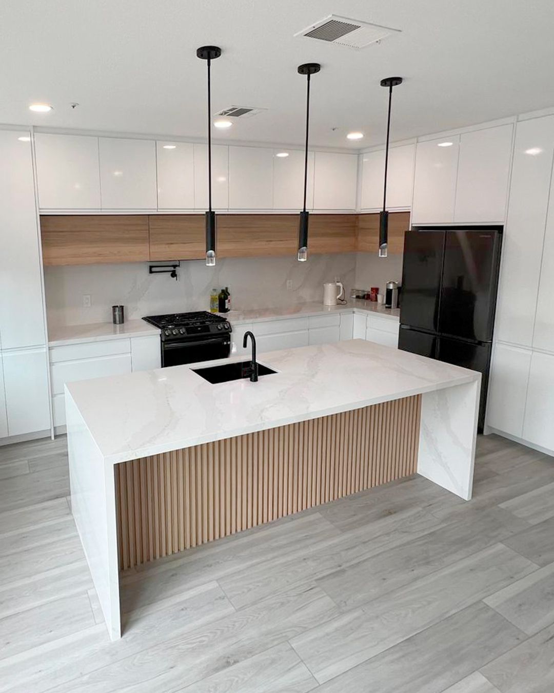 Modern kitchen with white cabinets, wood accents, and a large island with three pendant lights.