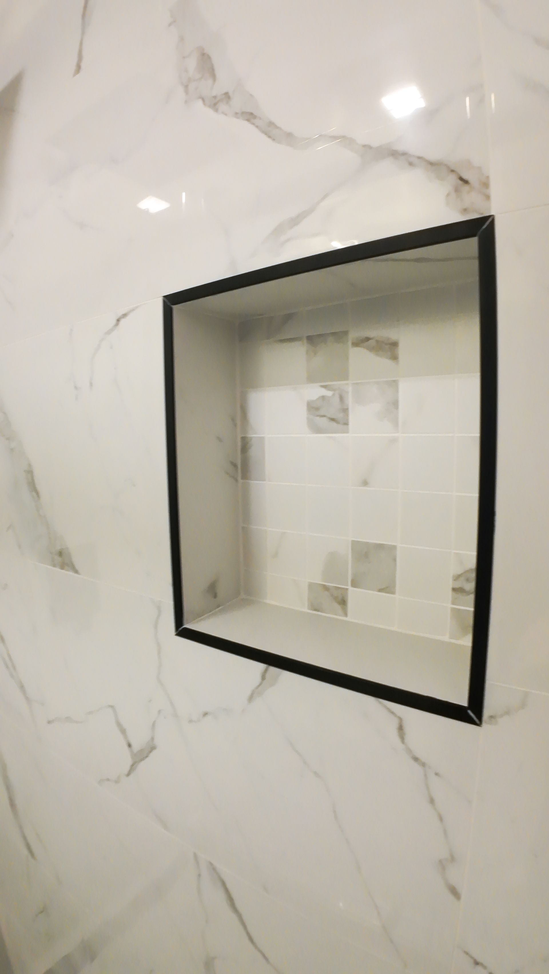 Square shower niche with black trim, built into a marble-patterned wall.