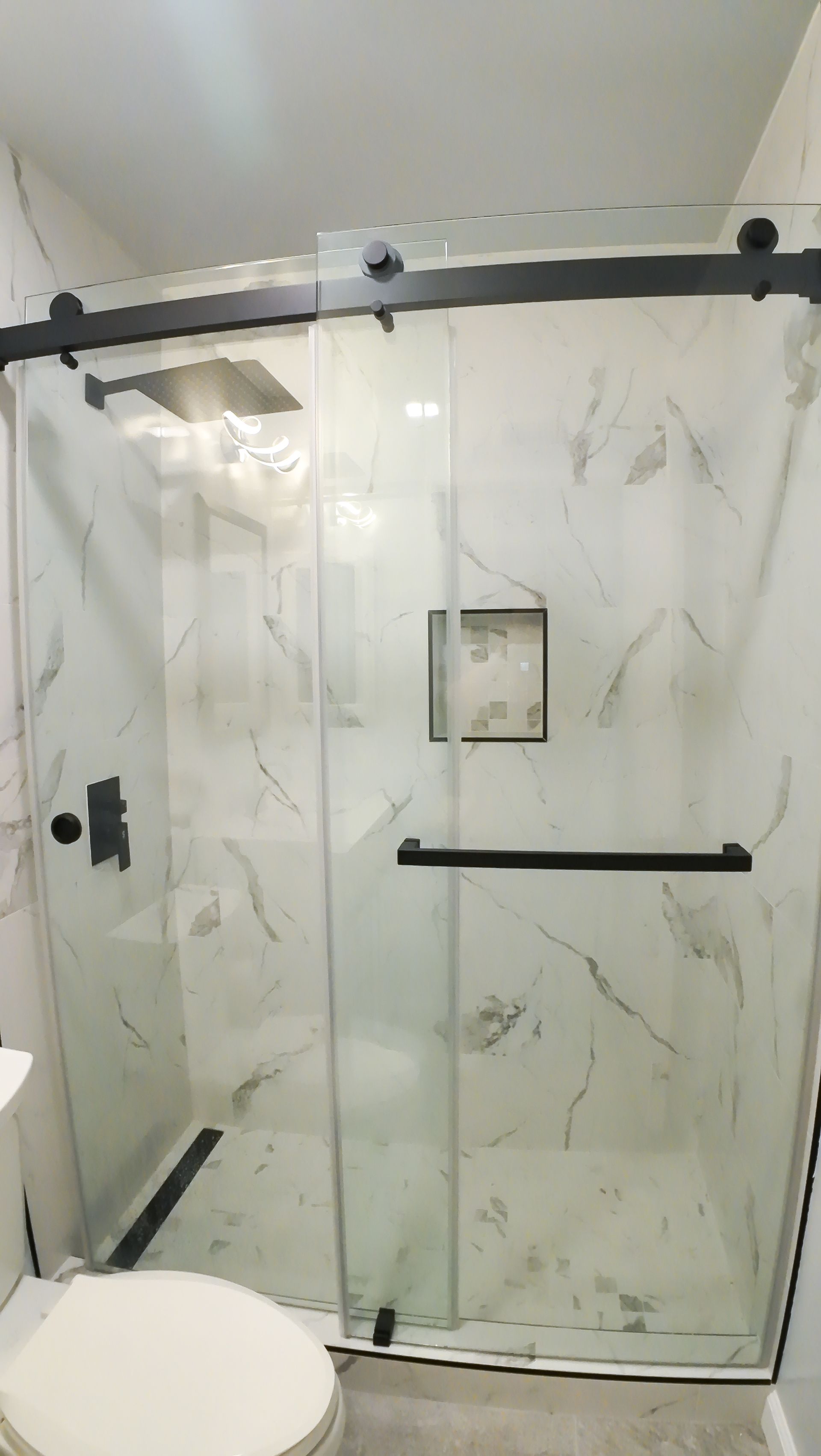 Shower enclosure with sliding glass doors, black hardware, and marble-look tile walls.