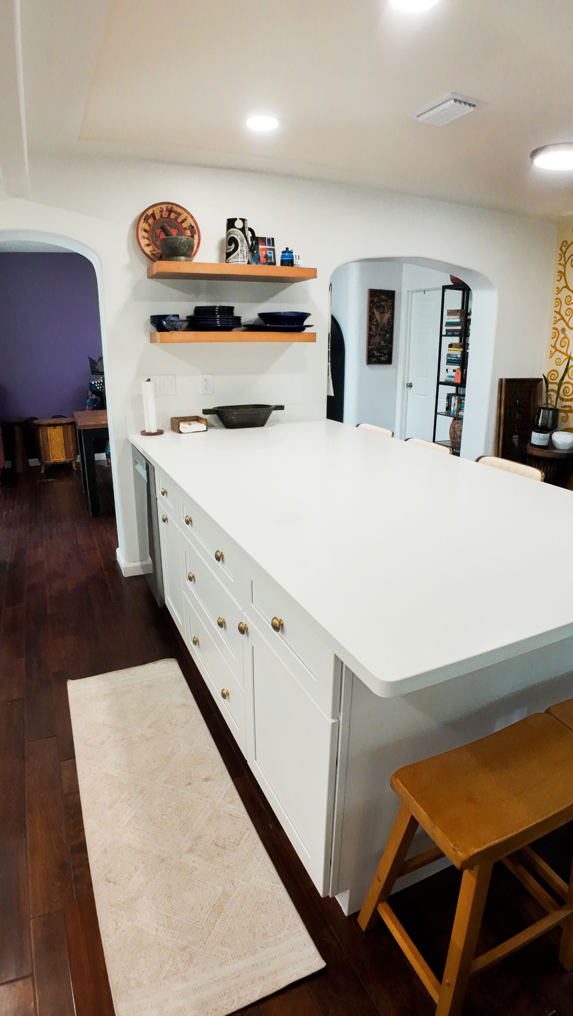 White kitchen island with white countertop, cabinets and brass hardware. Dark wood floors.
