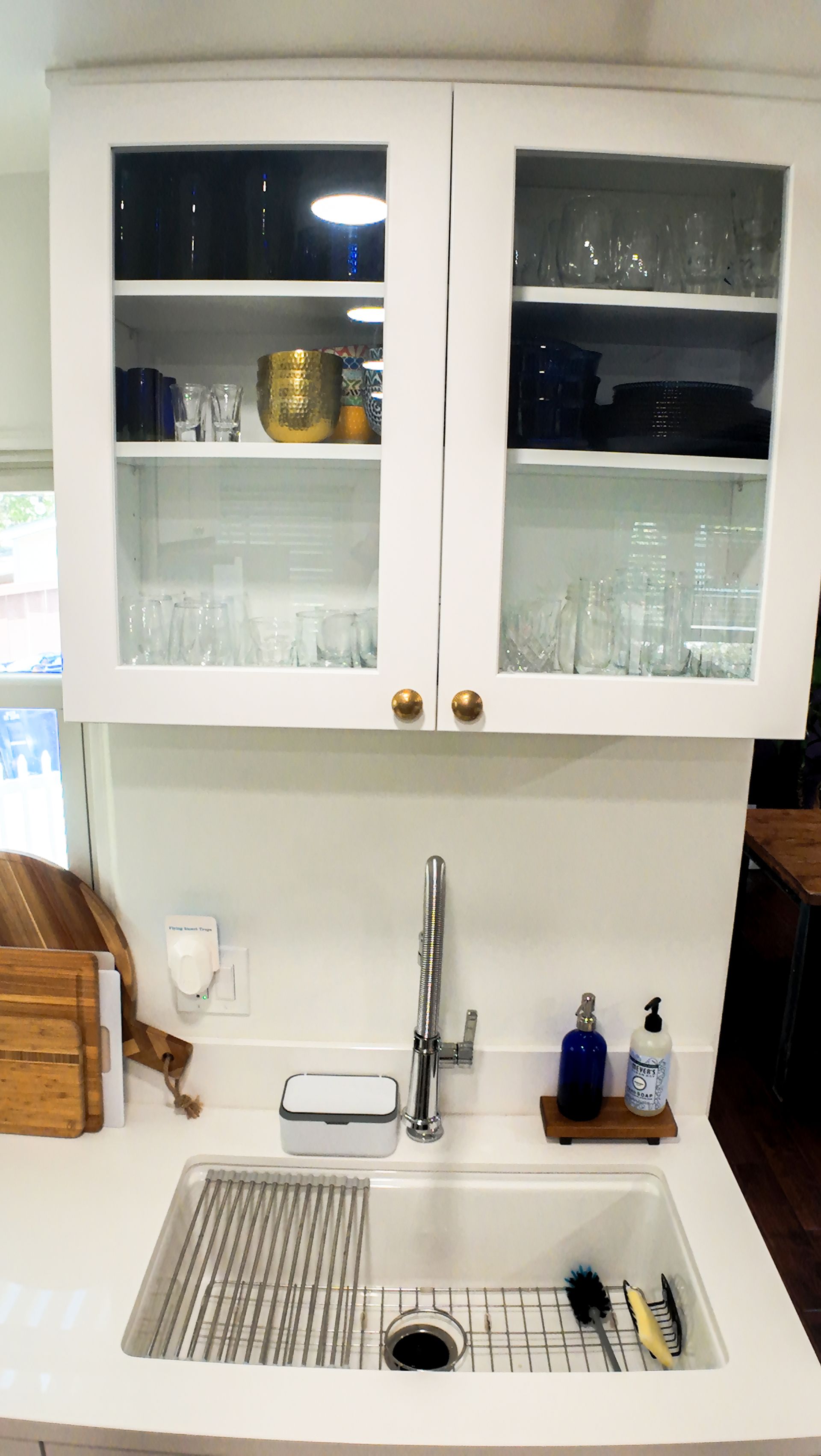 White kitchen cabinets above a sink with a metal drying rack.