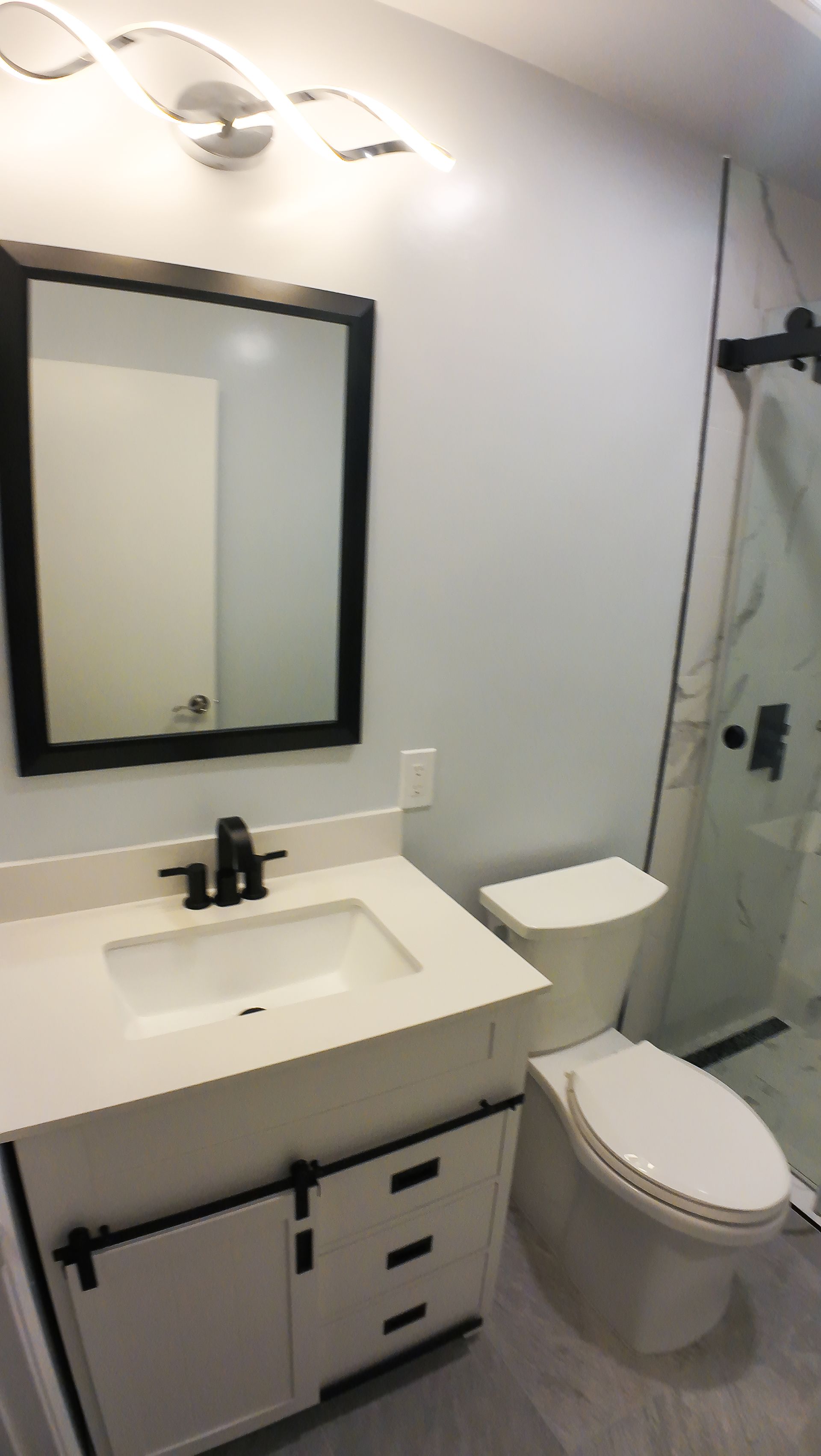 White bathroom with white vanity, black framed mirror, and sliding glass shower door.