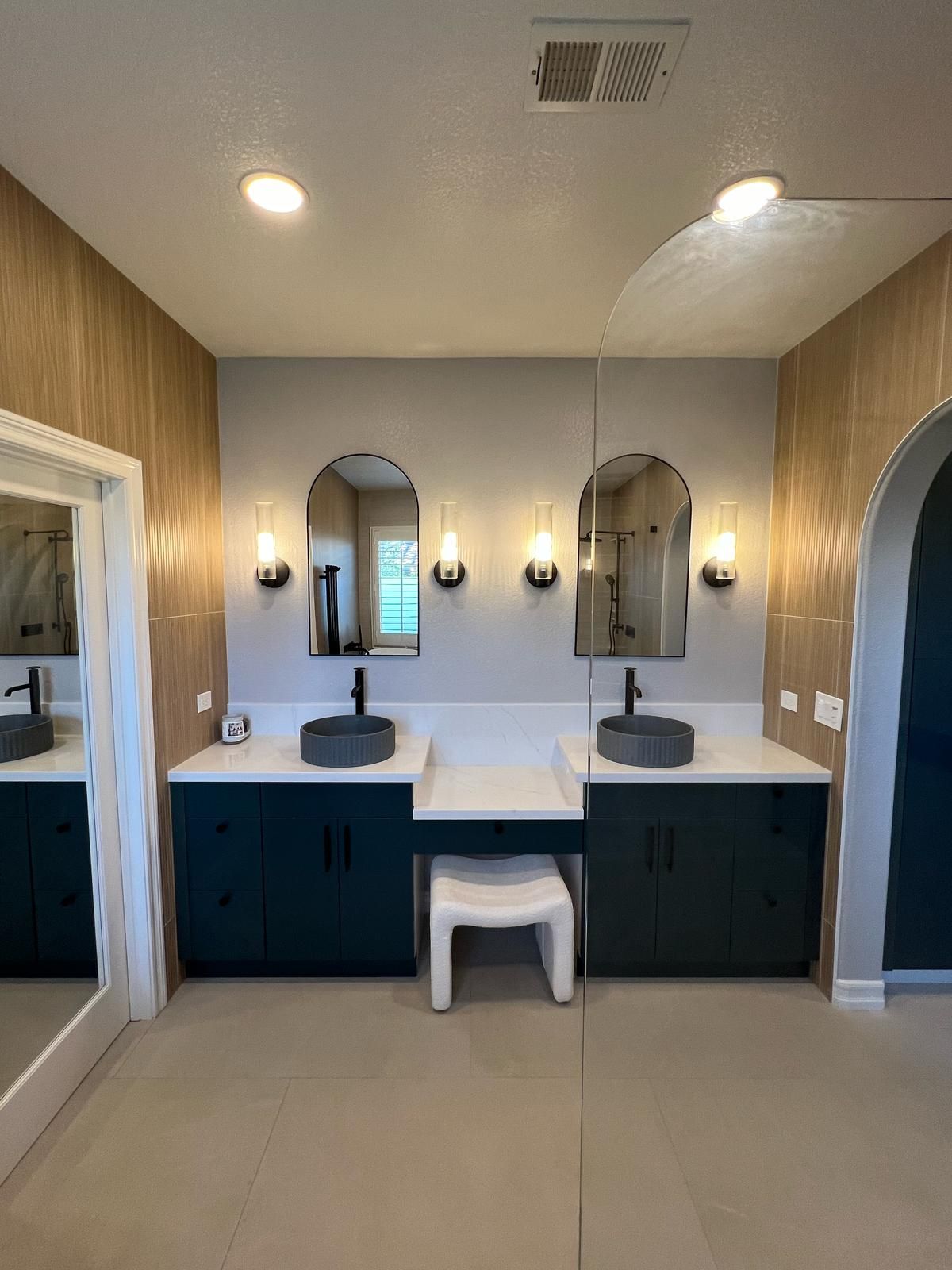 Modern bathroom with dual sinks, teal cabinets, arched mirrors, and wood accent wall.