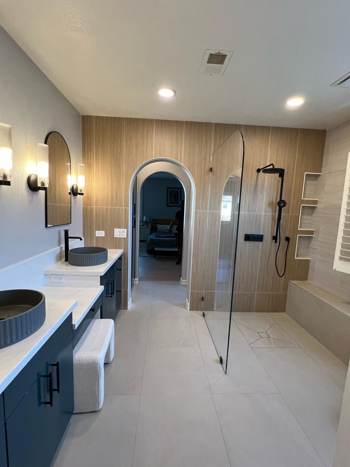 Modern bathroom with arches, blue cabinets, light tile, and a glass shower.