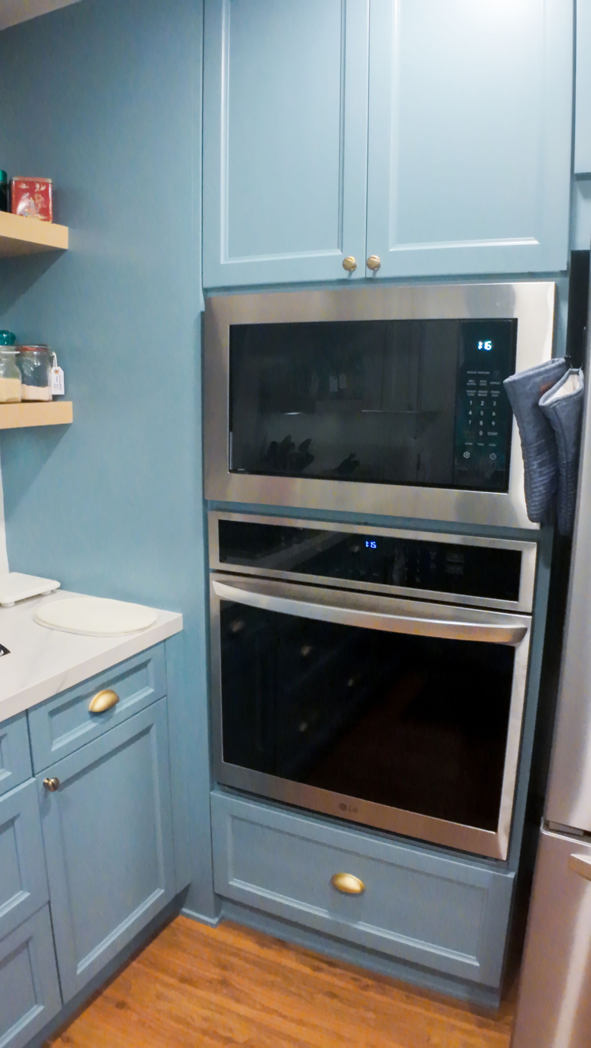 Blue kitchen cabinets with built-in stainless steel microwave and oven, gold hardware.