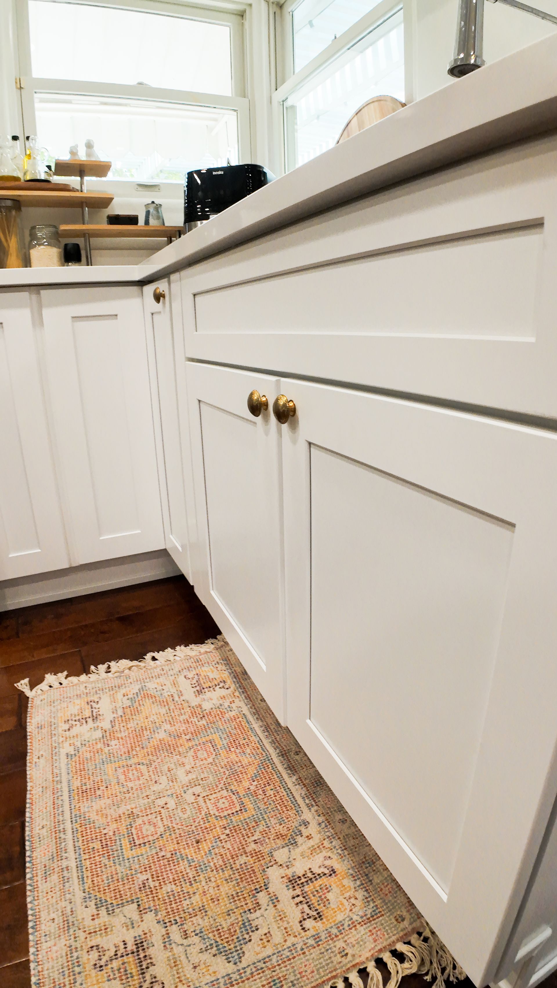 White kitchen cabinets with brass knobs, small rug, and countertop.